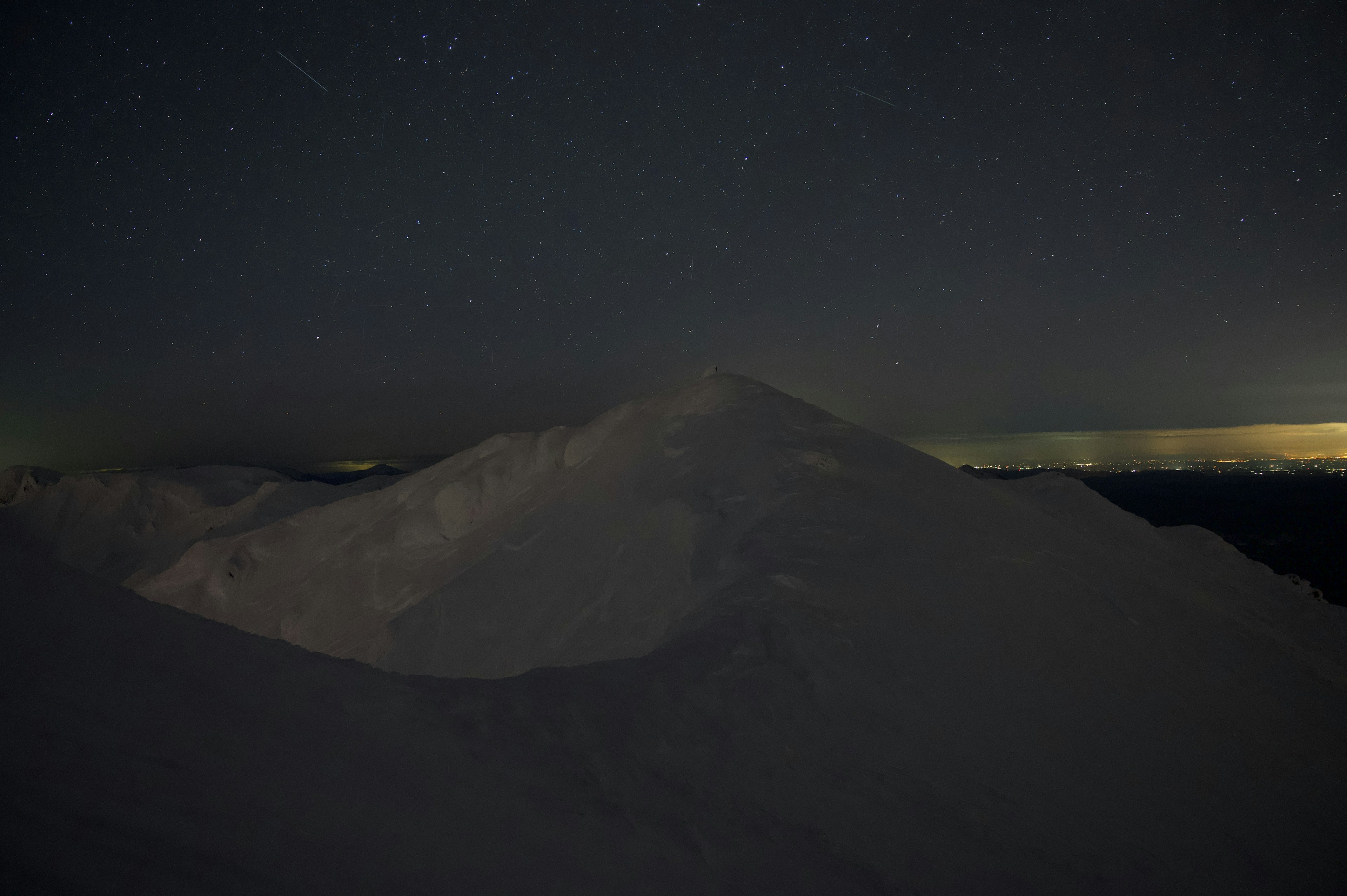 Silhouette of a snow-covered mountain against a dark night sky