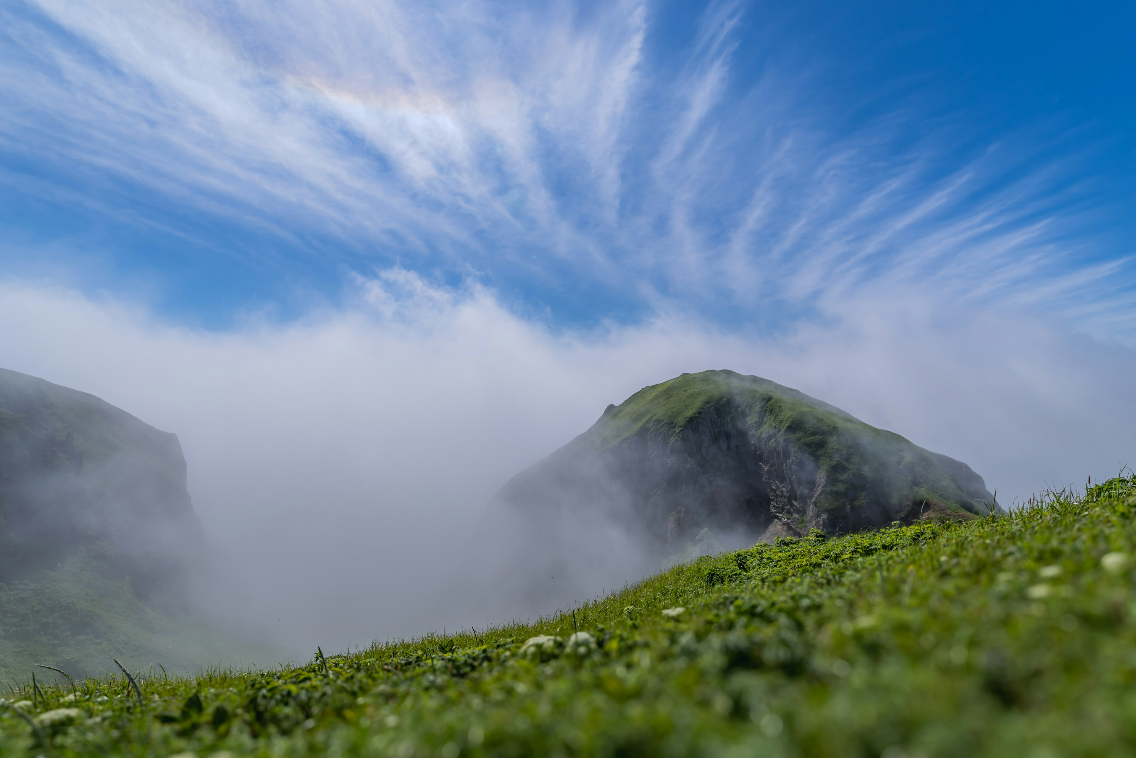 青い空と雲が広がる山の風景 緑の草原と霧に覆われた山々