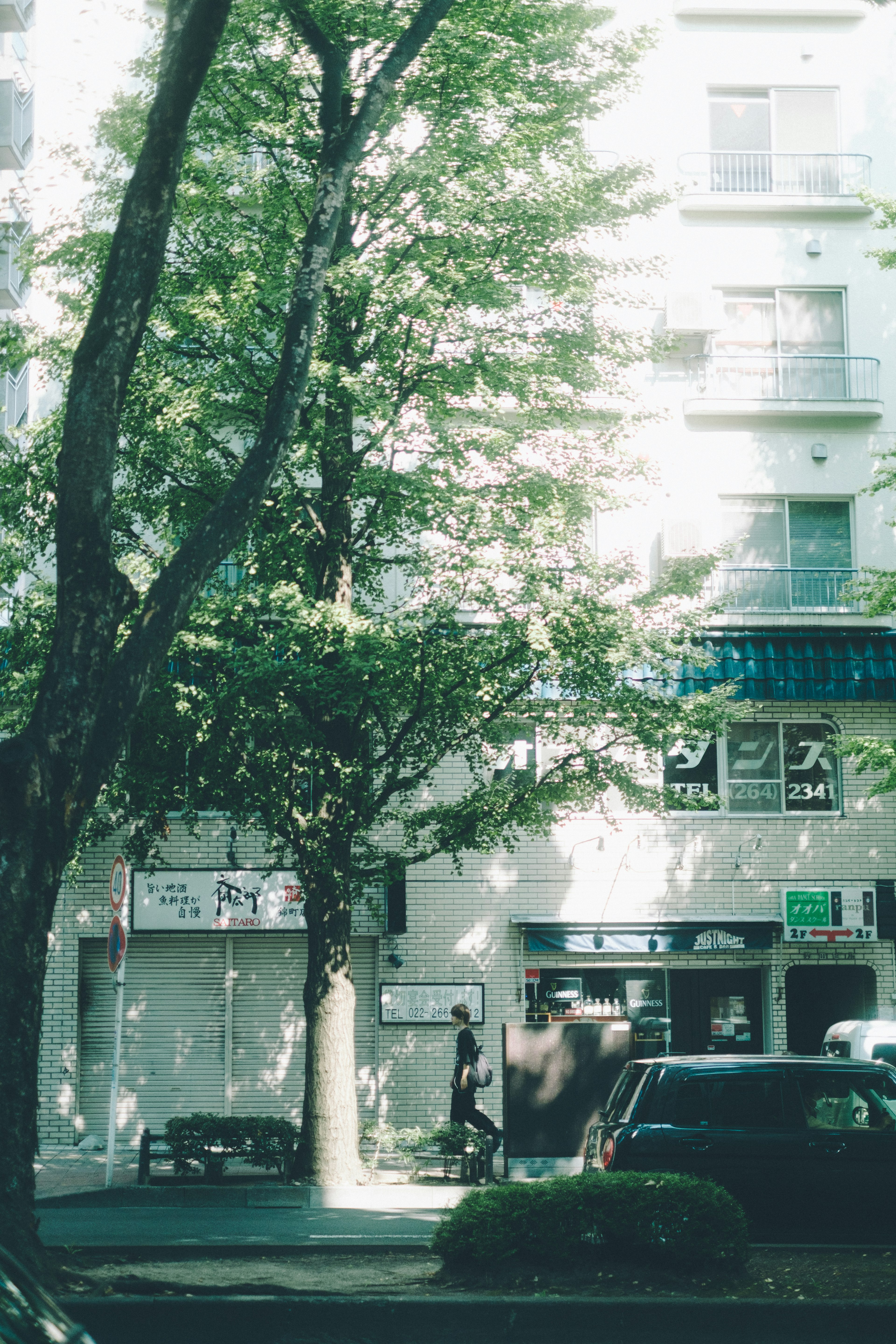 Building exterior surrounded by lush greenery and a passerby