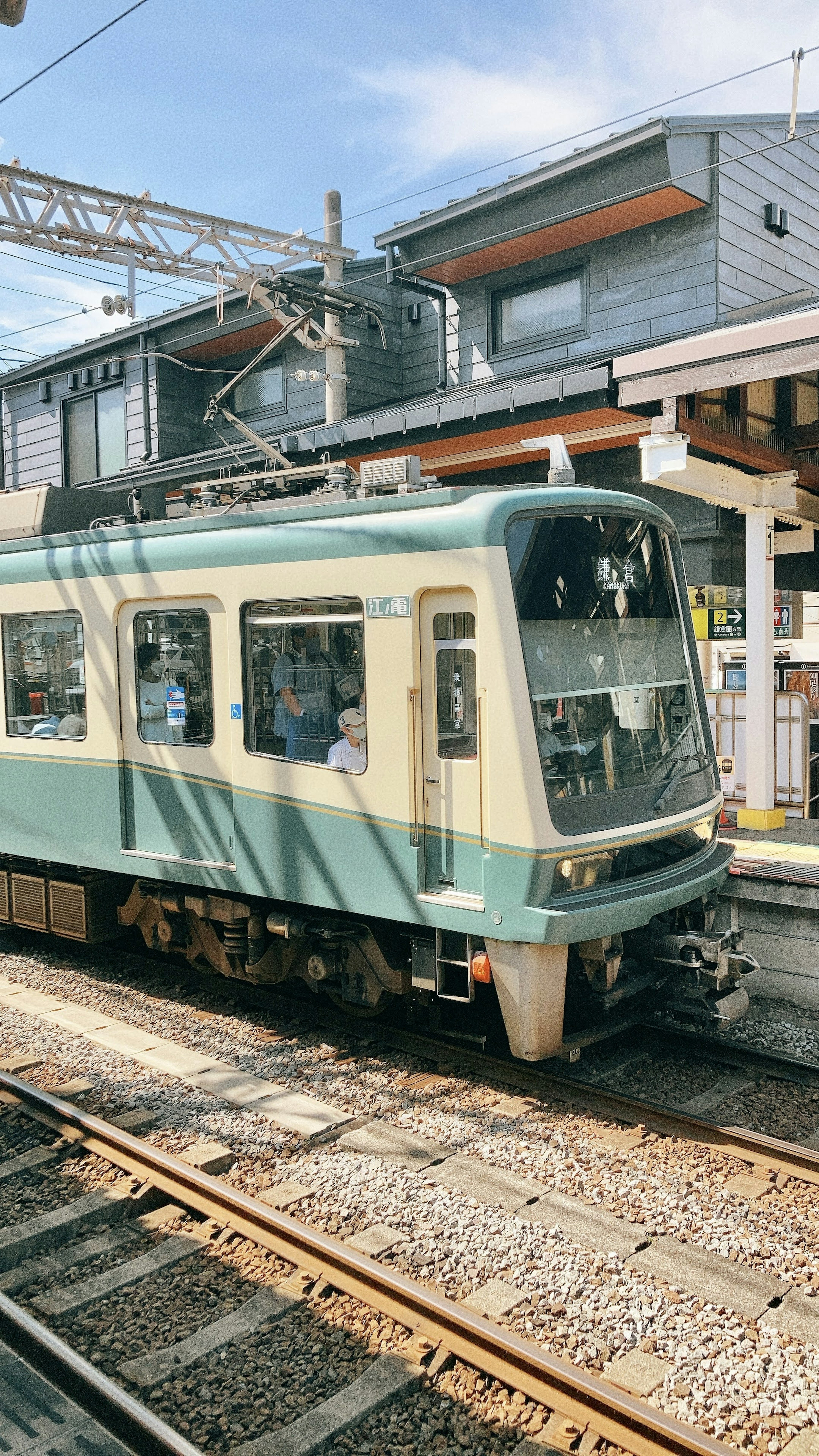 A teal train stopped at a station with a clear sky