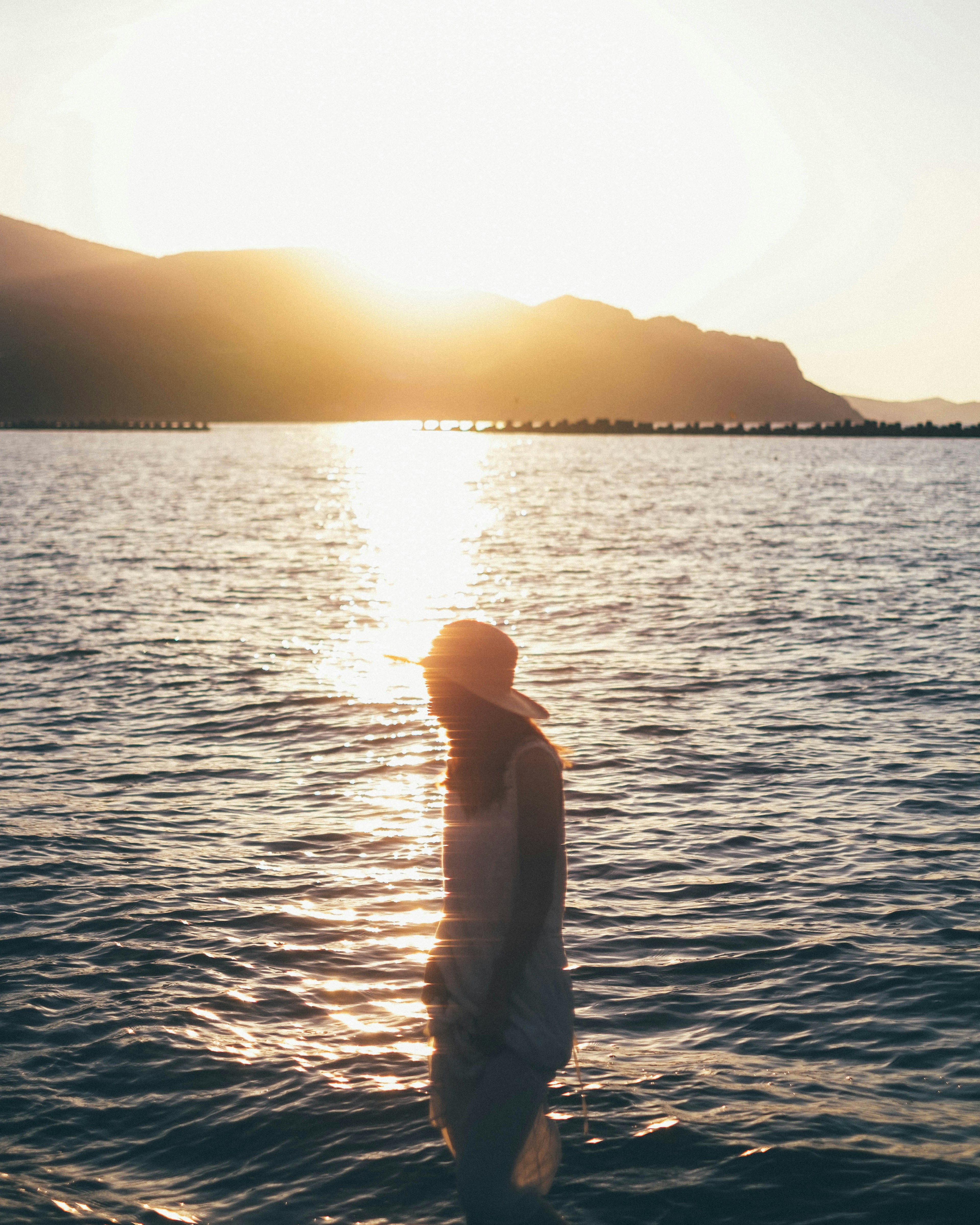 Una persona de pie junto al agua con el atardecer al fondo