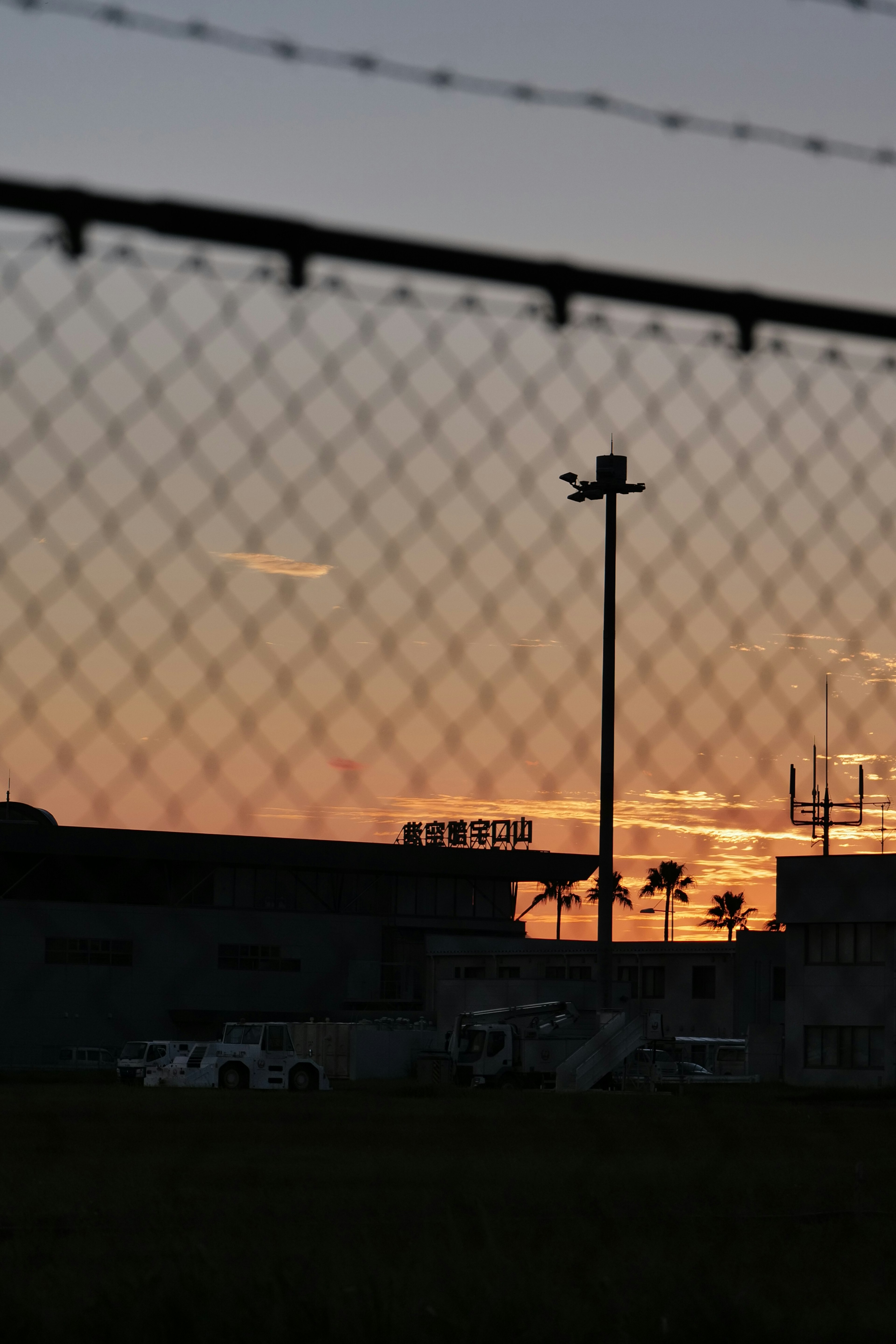 Silueta de un edificio y una cerca contra un cielo de atardecer