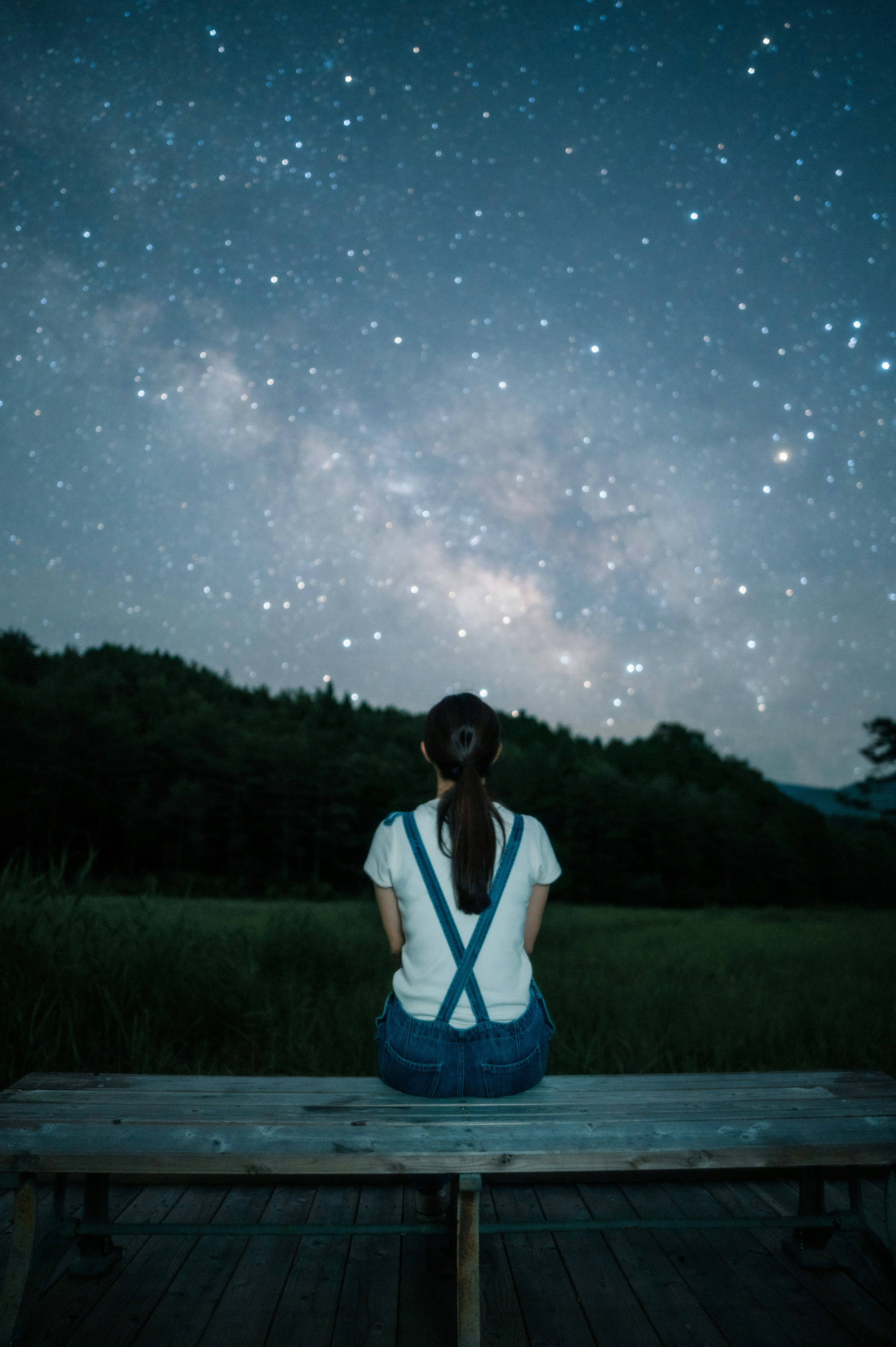 星空を見上げる女性がベンチに座っている風景