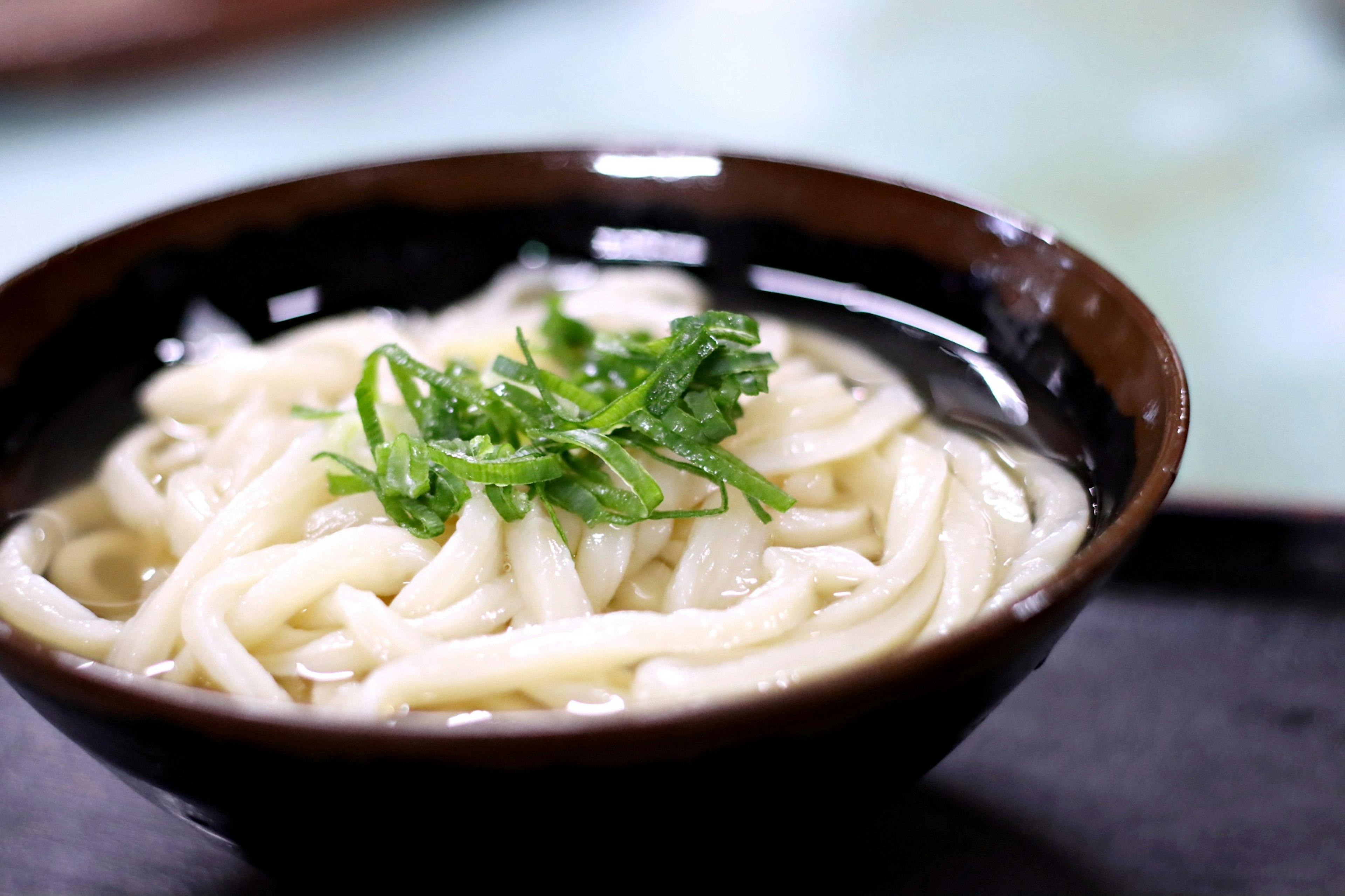 Udon-Nudeln in einer schwarzen Schüssel mit Frühlingszwiebelgarnitur serviert