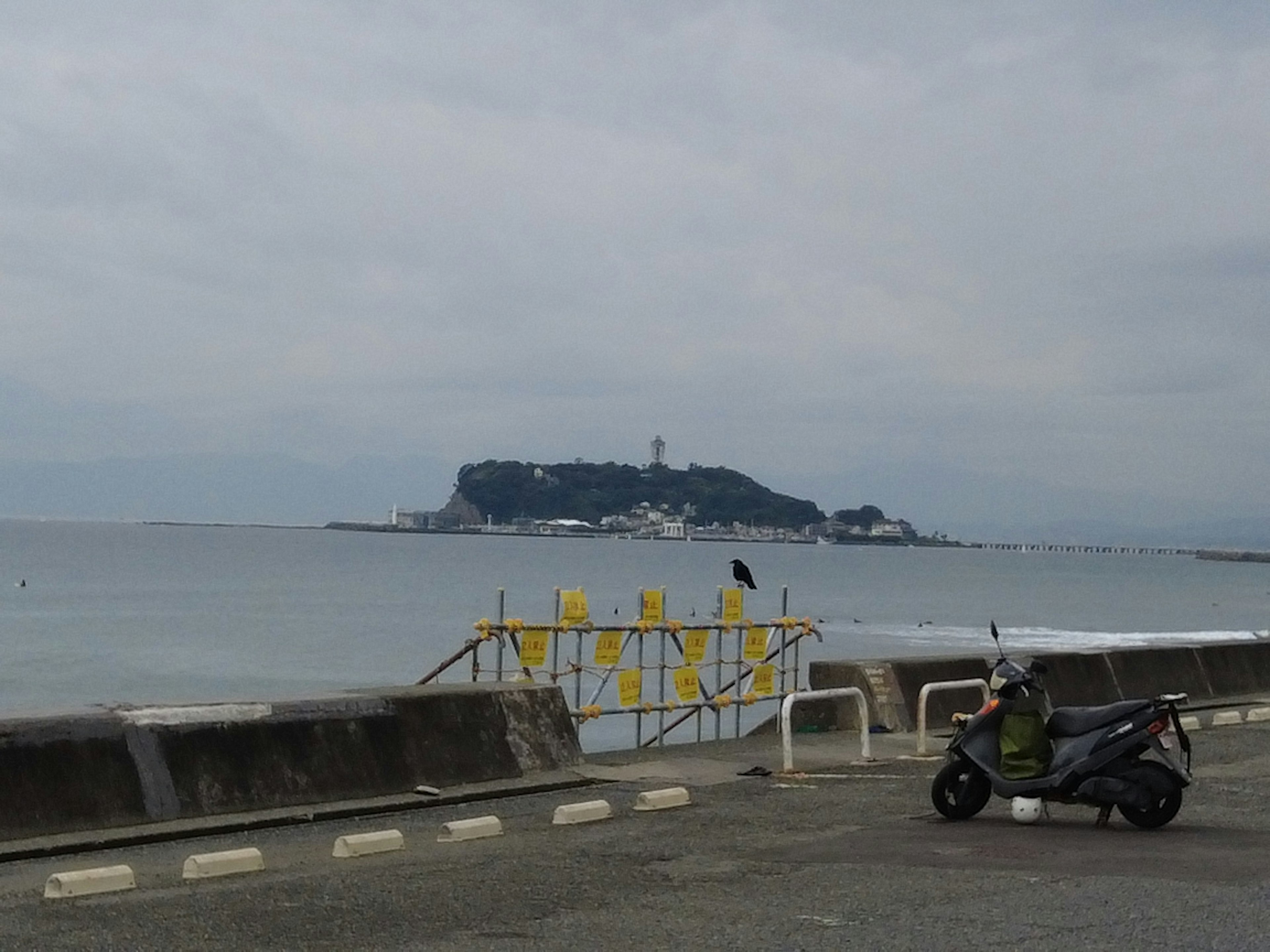 Vue côtière avec une moto au premier plan et une île avec un phare au loin