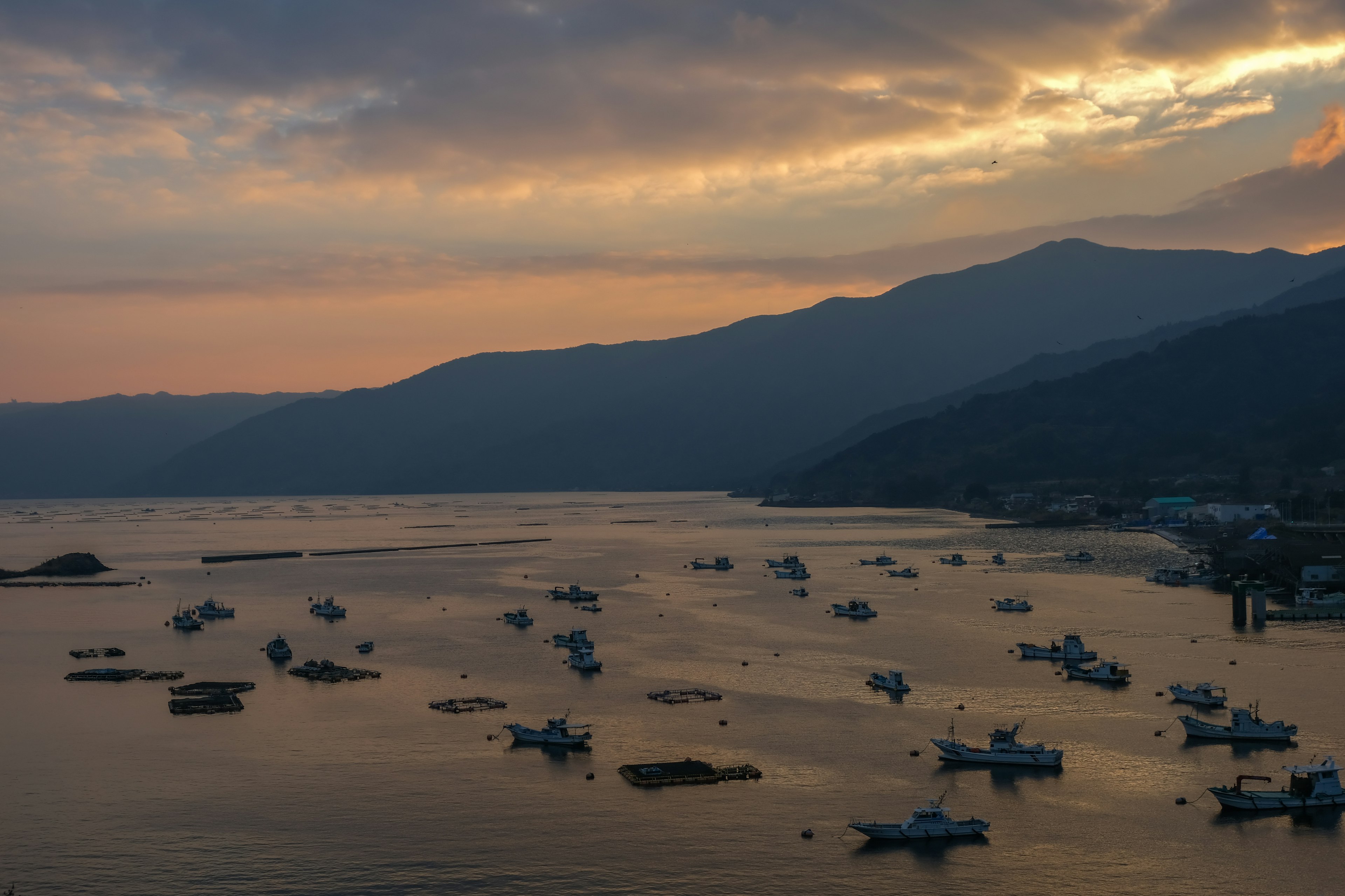 Botes flotando en un mar al atardecer con siluetas de montañas