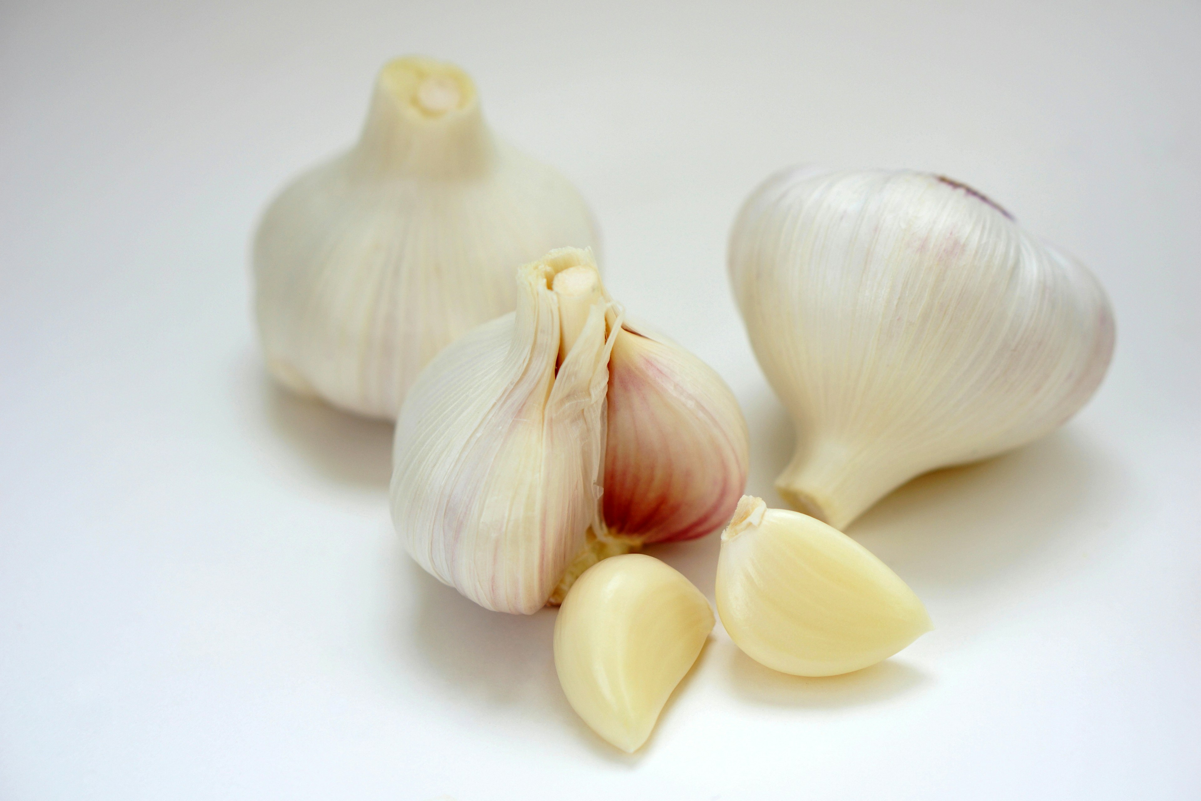 Three white garlic bulbs with peeled cloves scattered around