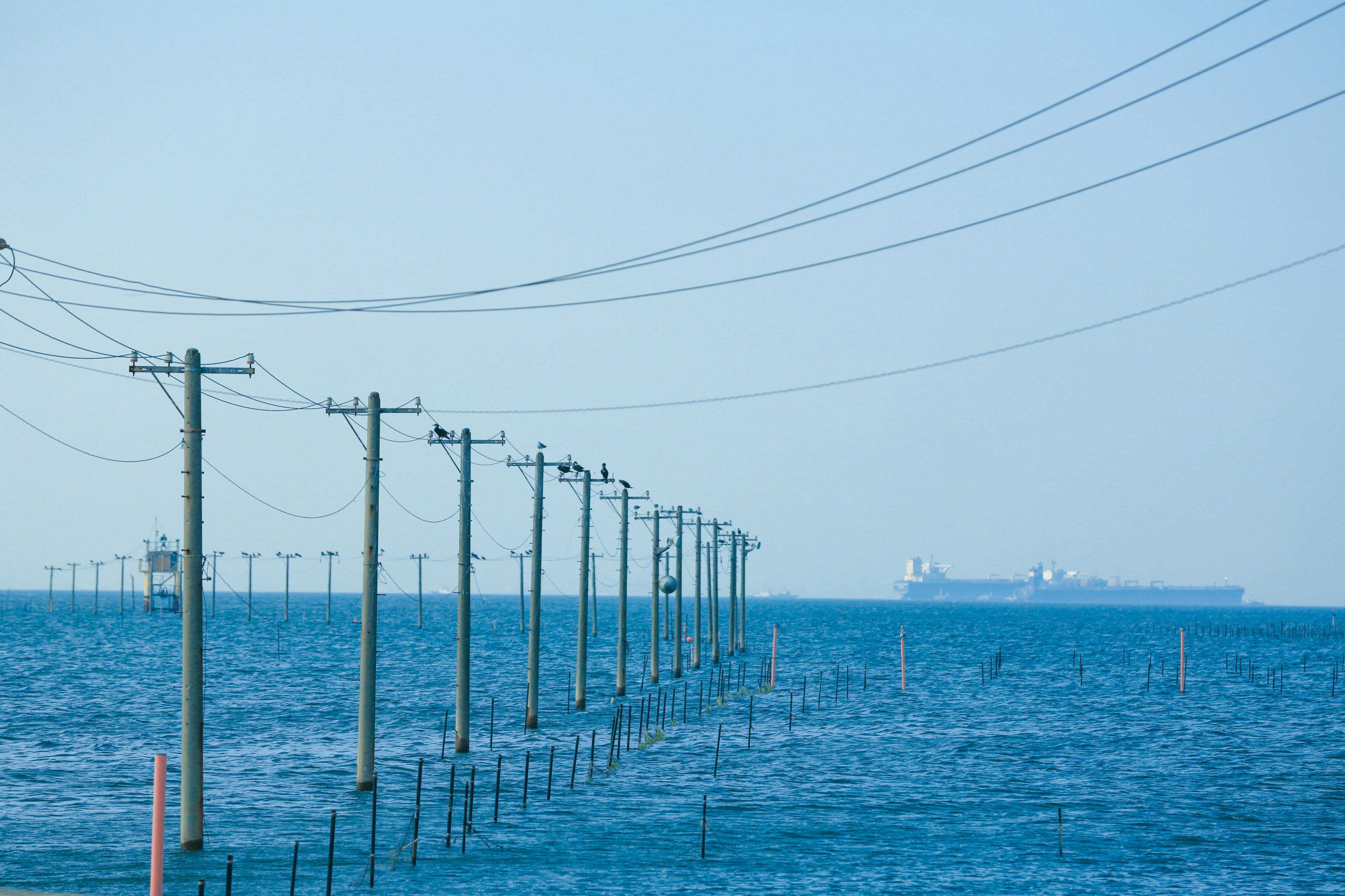 Vista di pali elettrici nel mare con una nave in lontananza