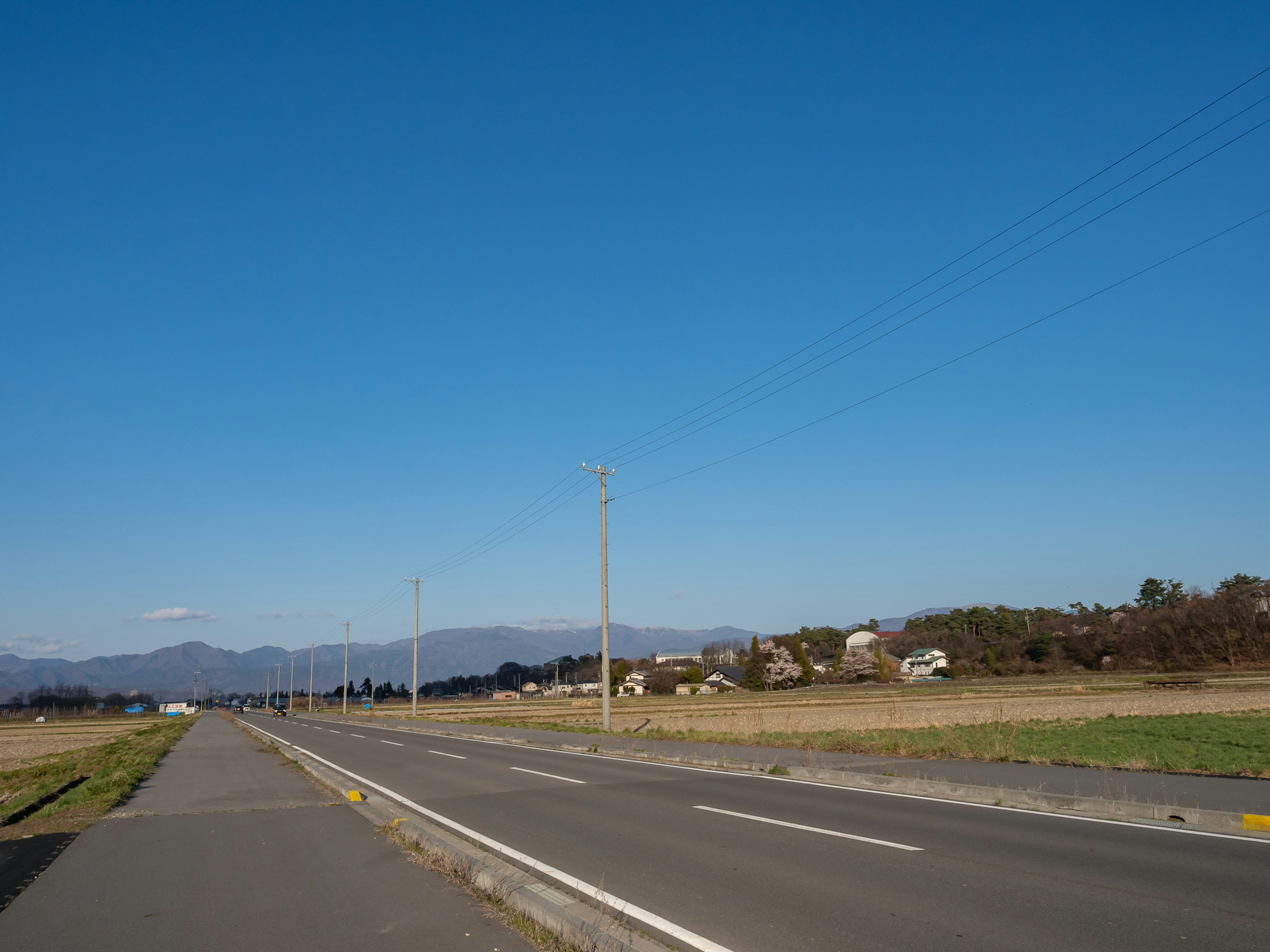 宽阔的道路在晴朗的蓝天下与乡村风景