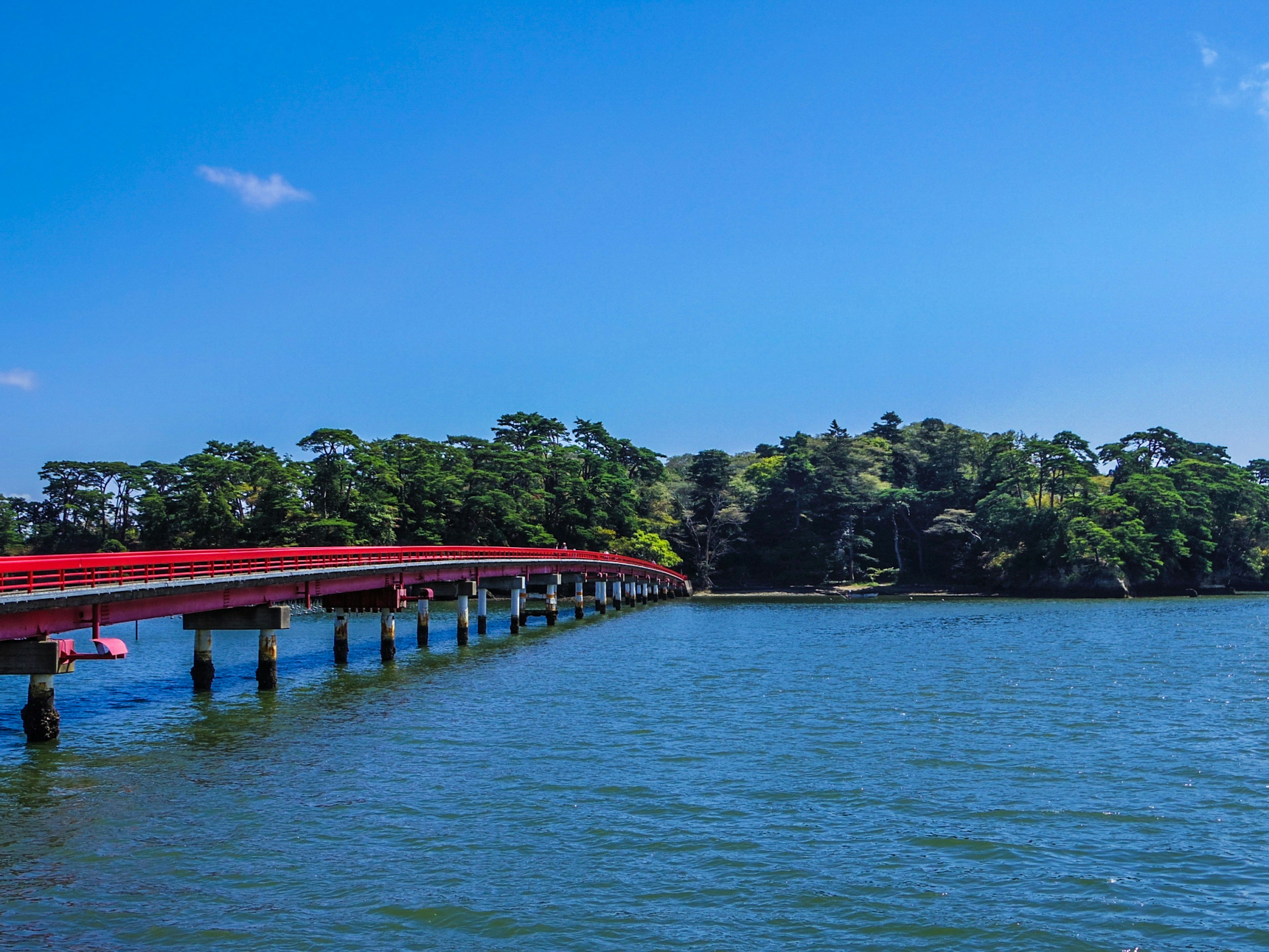 Un pont rouge s'étendant sur l'eau menant à une île verte