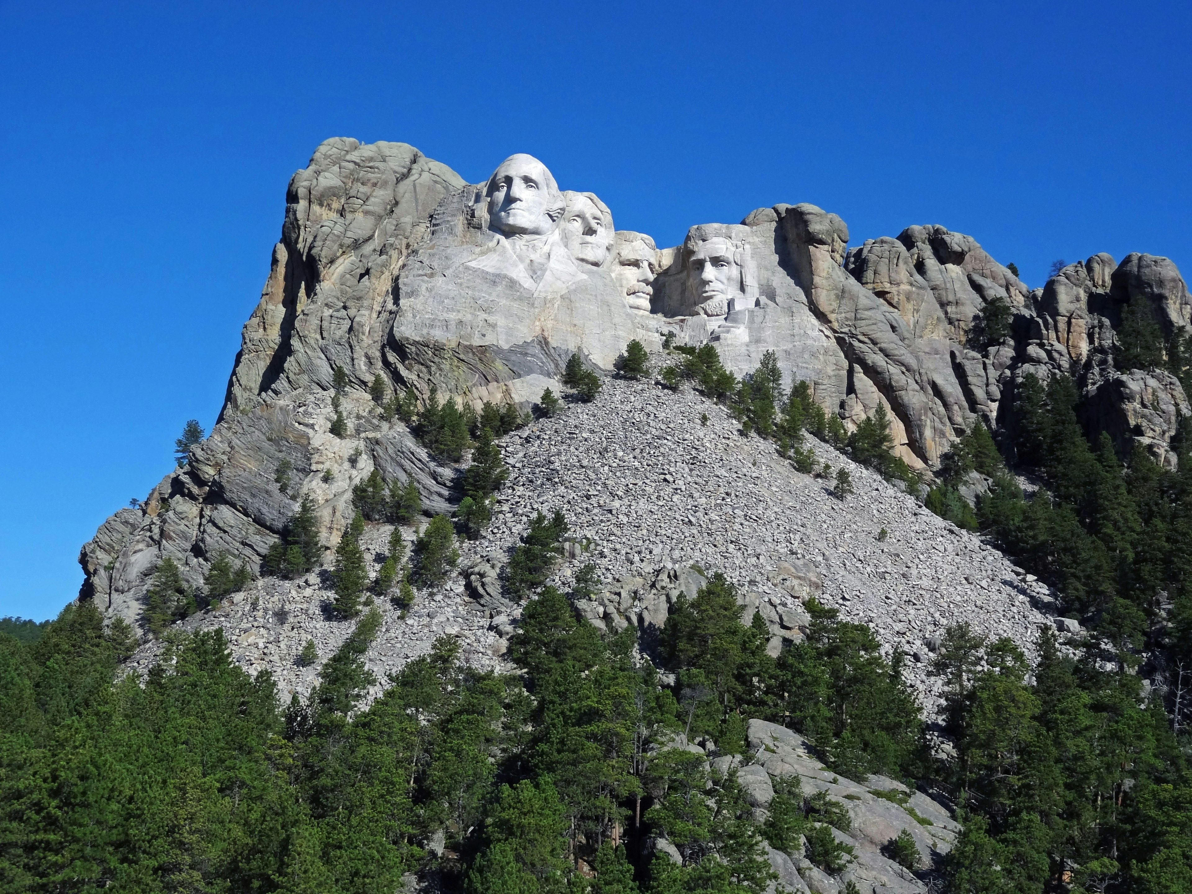 Tượng đài Mount Rushmore nhìn thấy trên cảnh quan núi cây xanh và bầu trời xanh