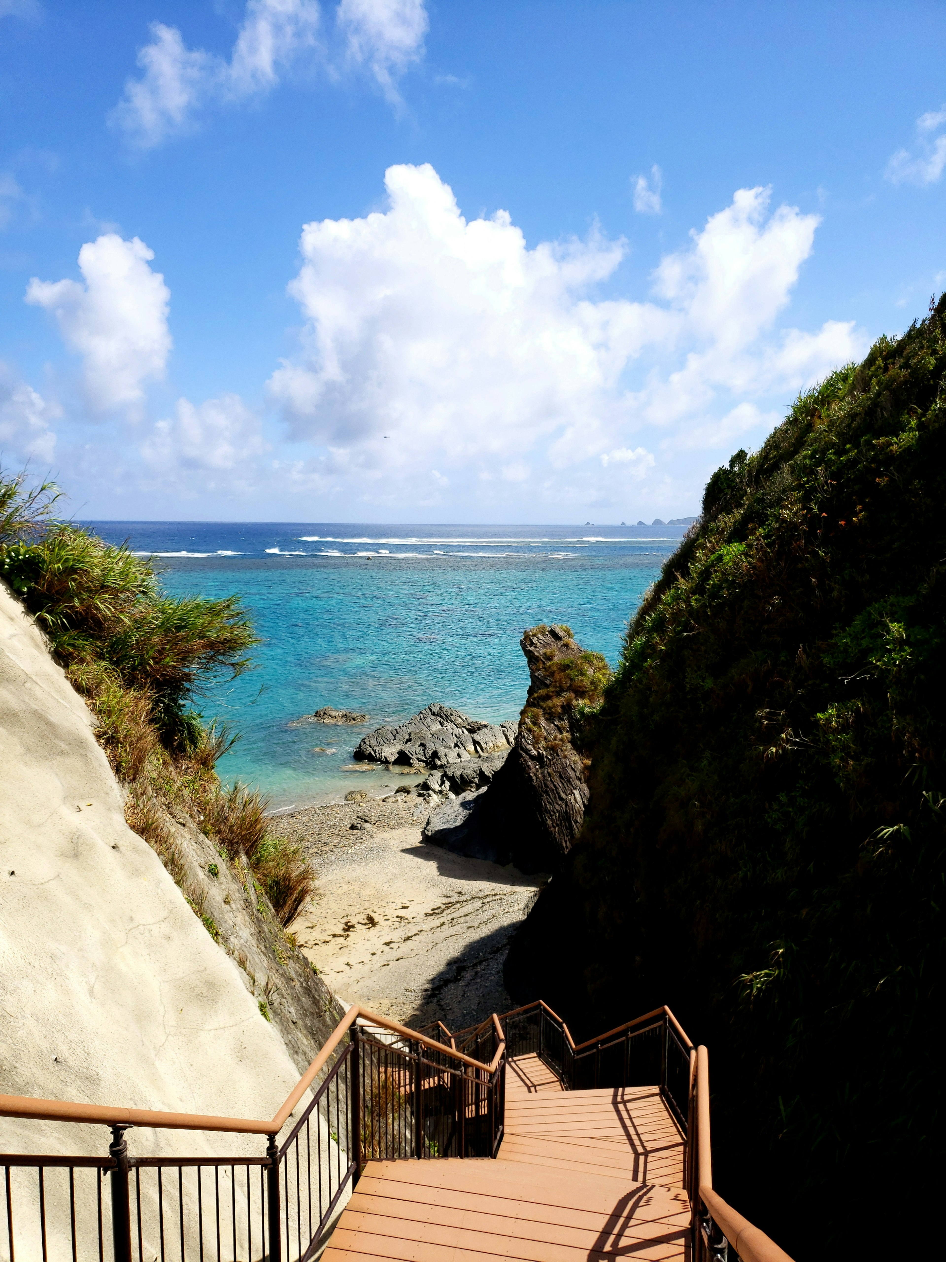 Scenic view of wooden steps leading to a beach with turquoise waters and a blue sky