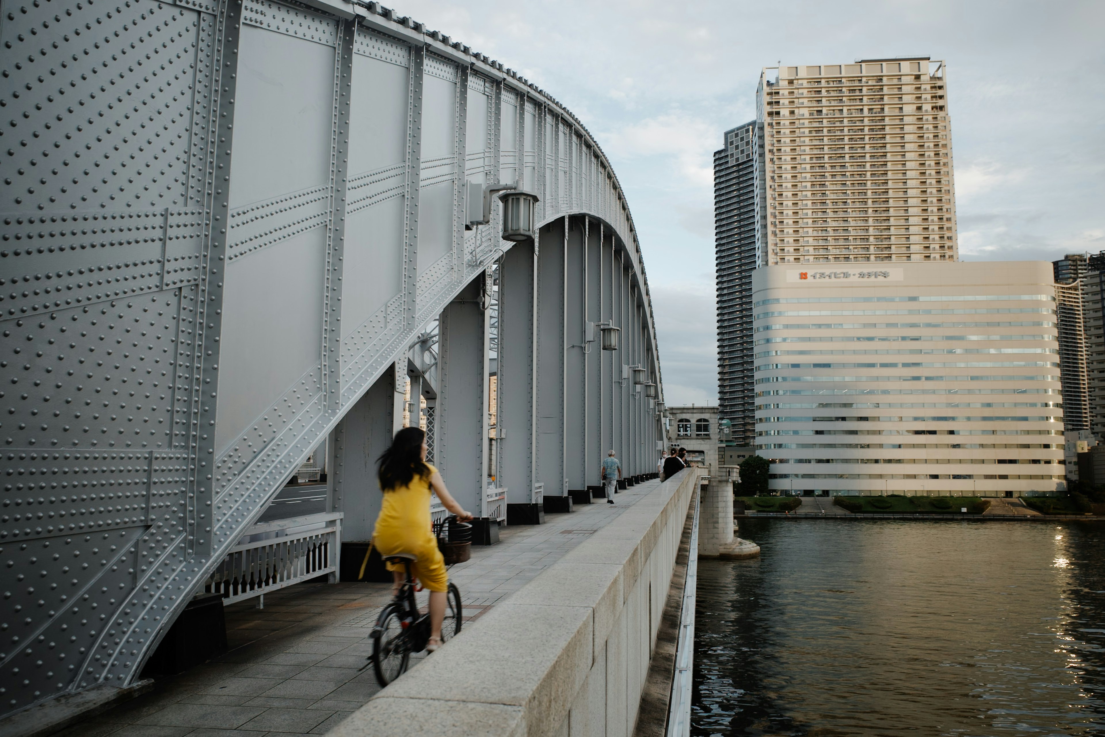 Femme en robe jaune faisant du vélo le long d'un pont au bord de l'eau