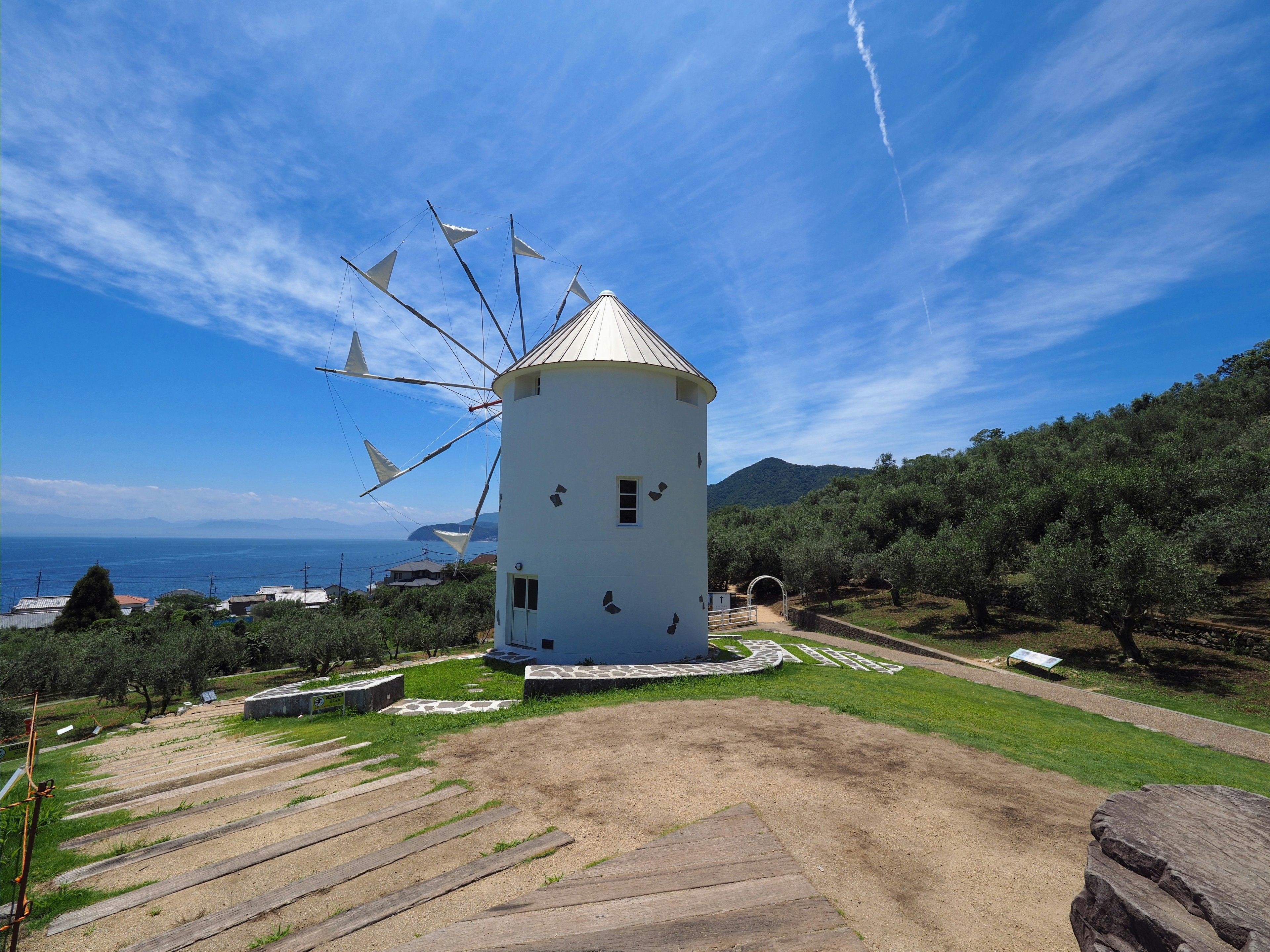 Moulin blanc sous un ciel bleu entouré d'oliviers