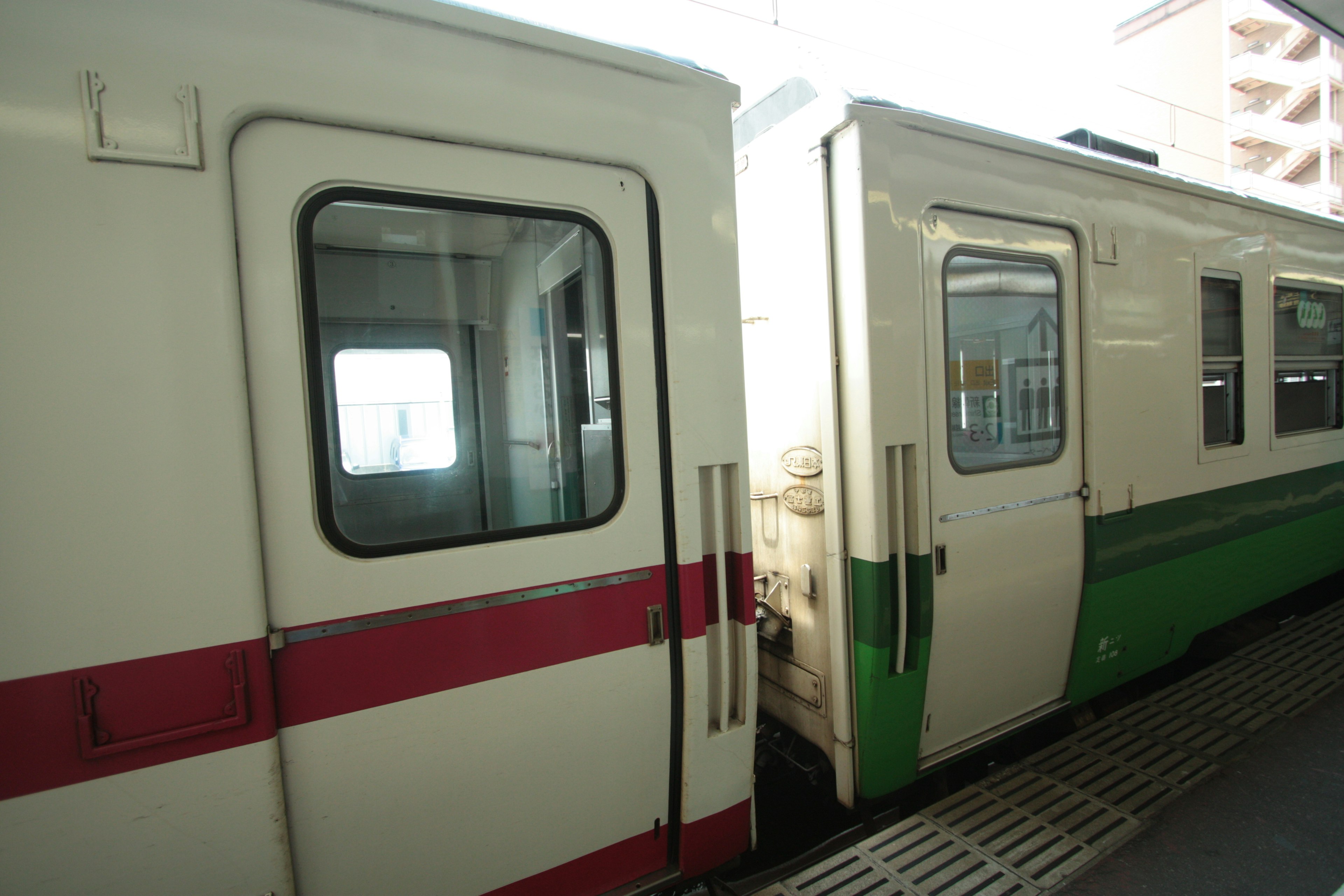 Weißer Zug mit rotem Streifen und grüner Zug an einem Bahnhof