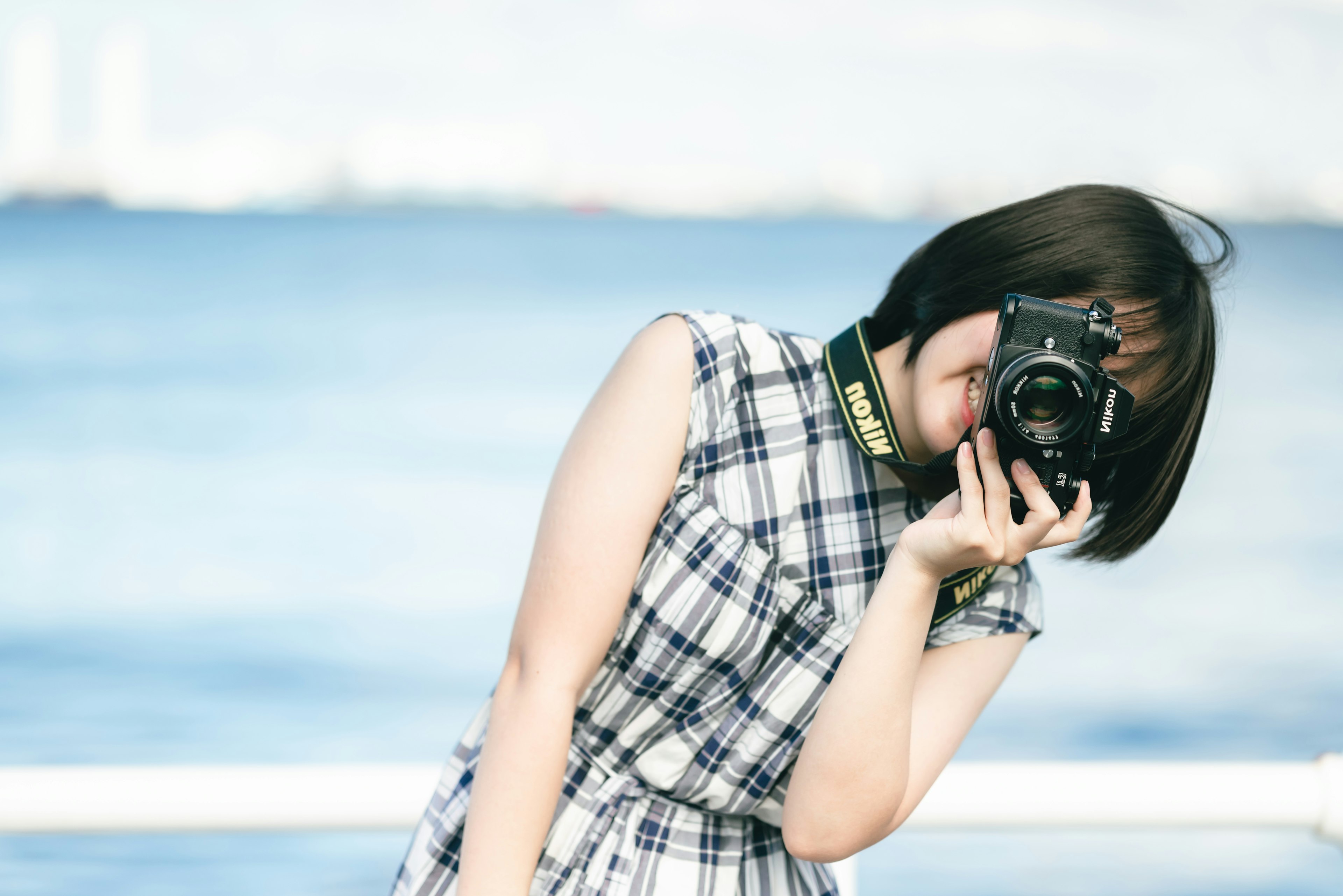 Woman smiling while holding a camera with the sea in the background