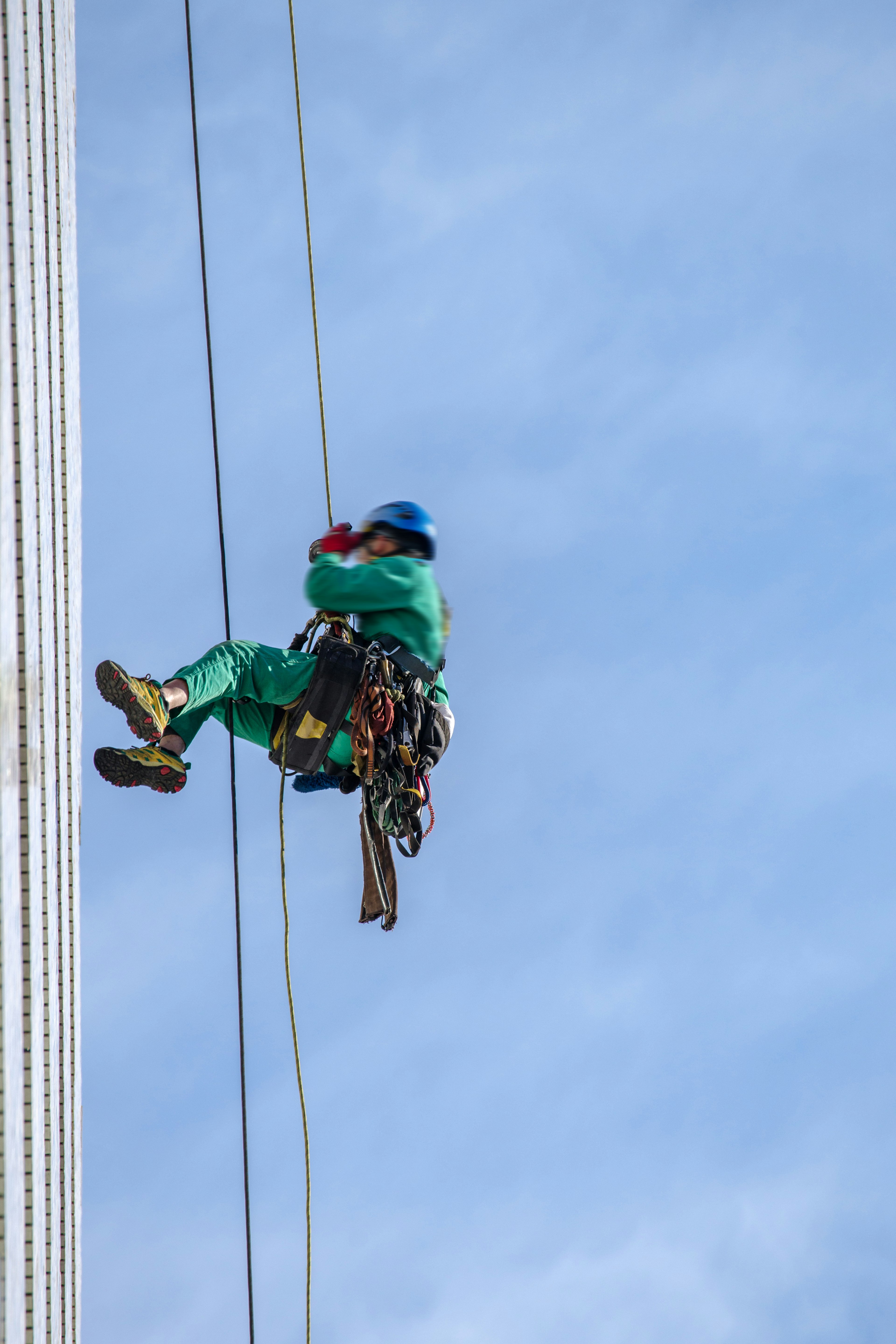 Ouvrier grimpant sur l'extérieur d'un immeuble de grande hauteur portant des vêtements de travail verts et un casque