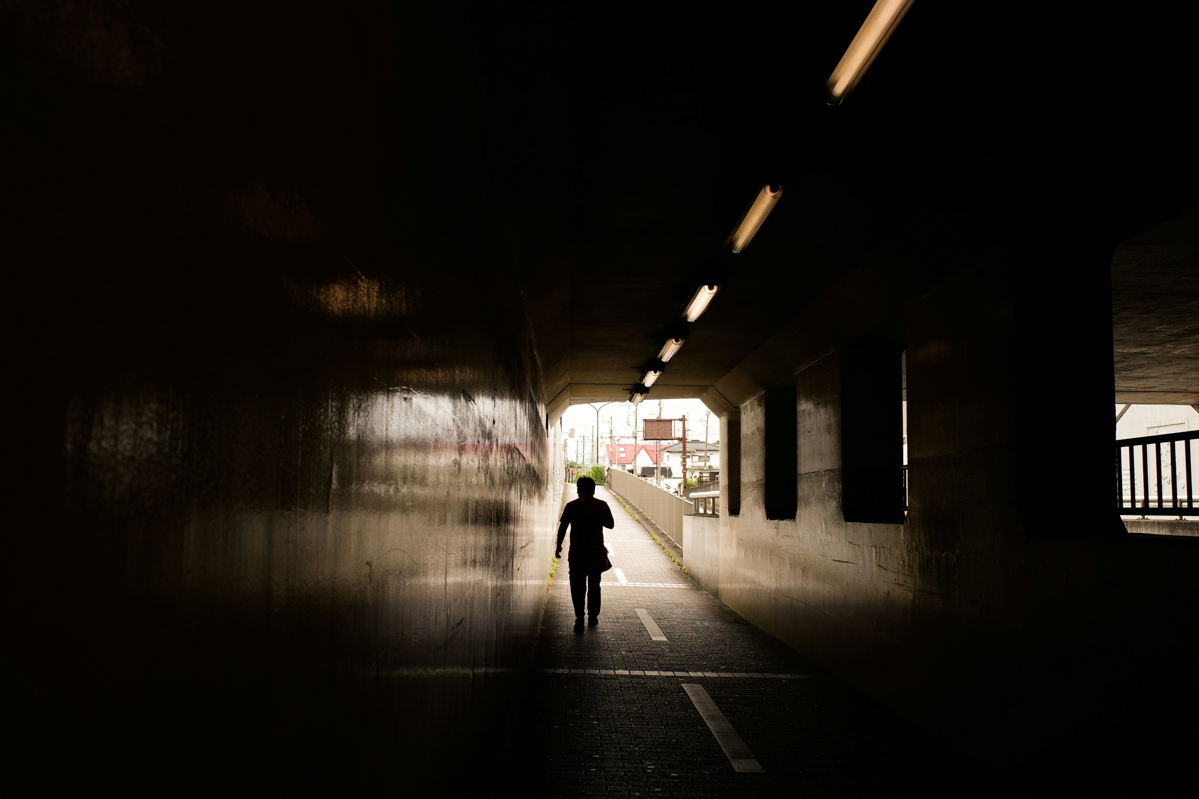 A silhouette of a person walking through a dark tunnel with a bright exit