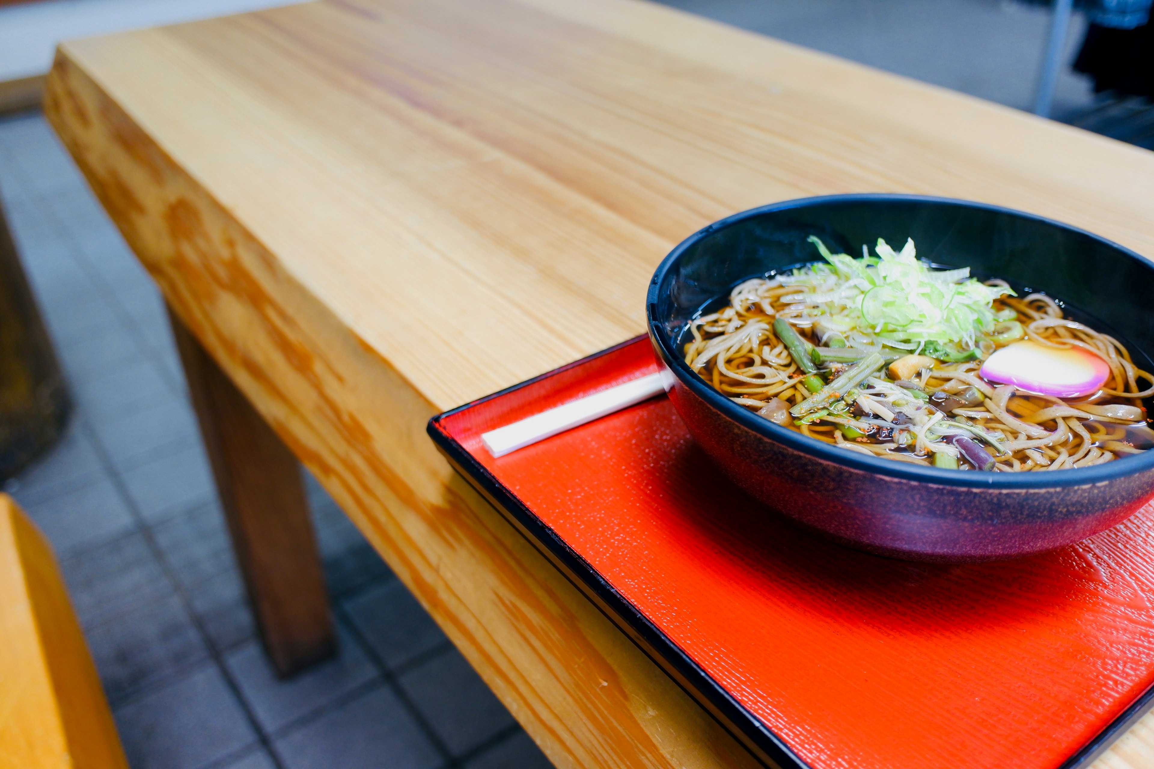 木製のテーブルの上にあるラーメンのボウルと赤いトレイ