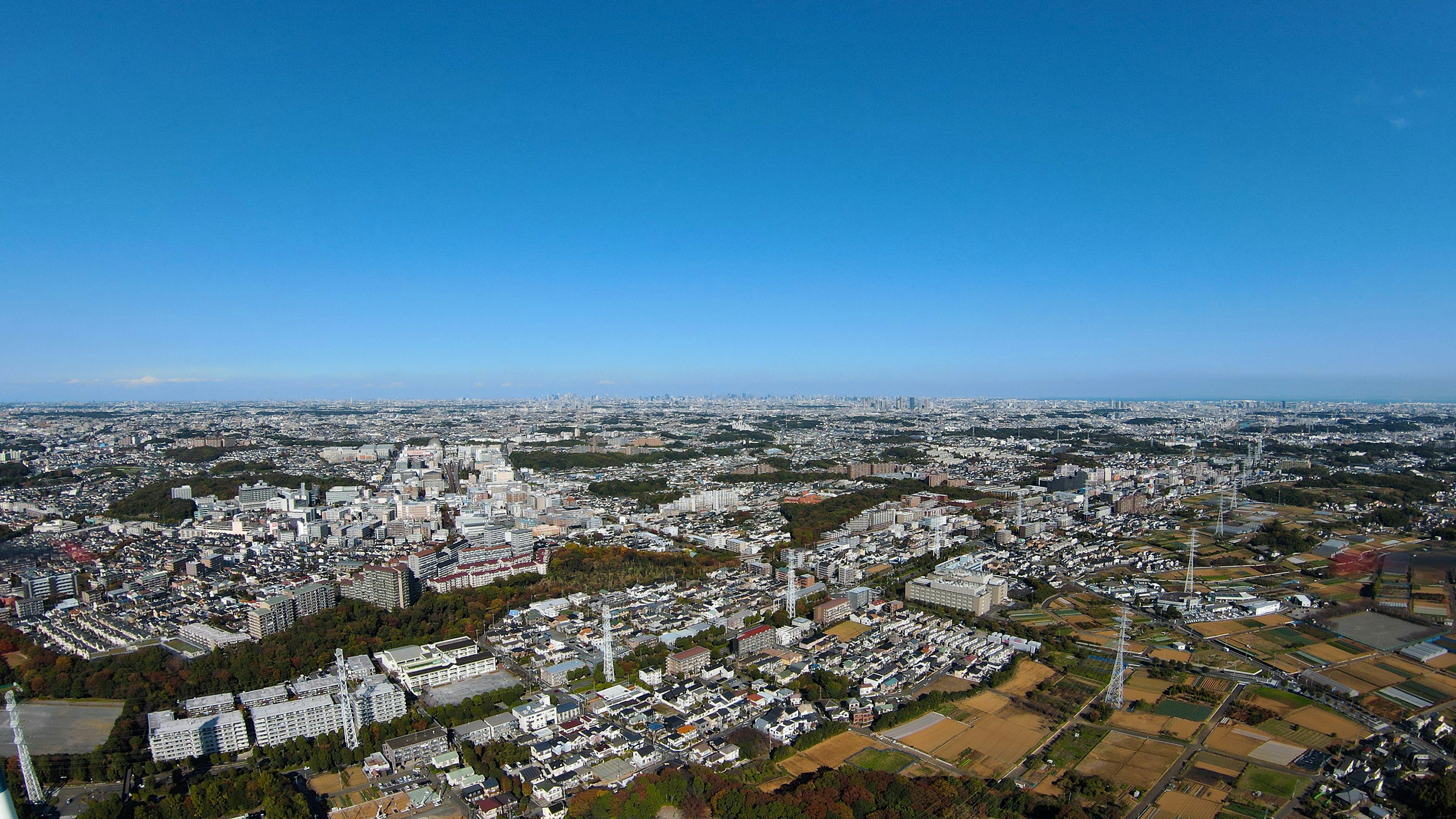 Pemandangan panorama kota yang luas di bawah langit biru dengan bangunan dan area hijau