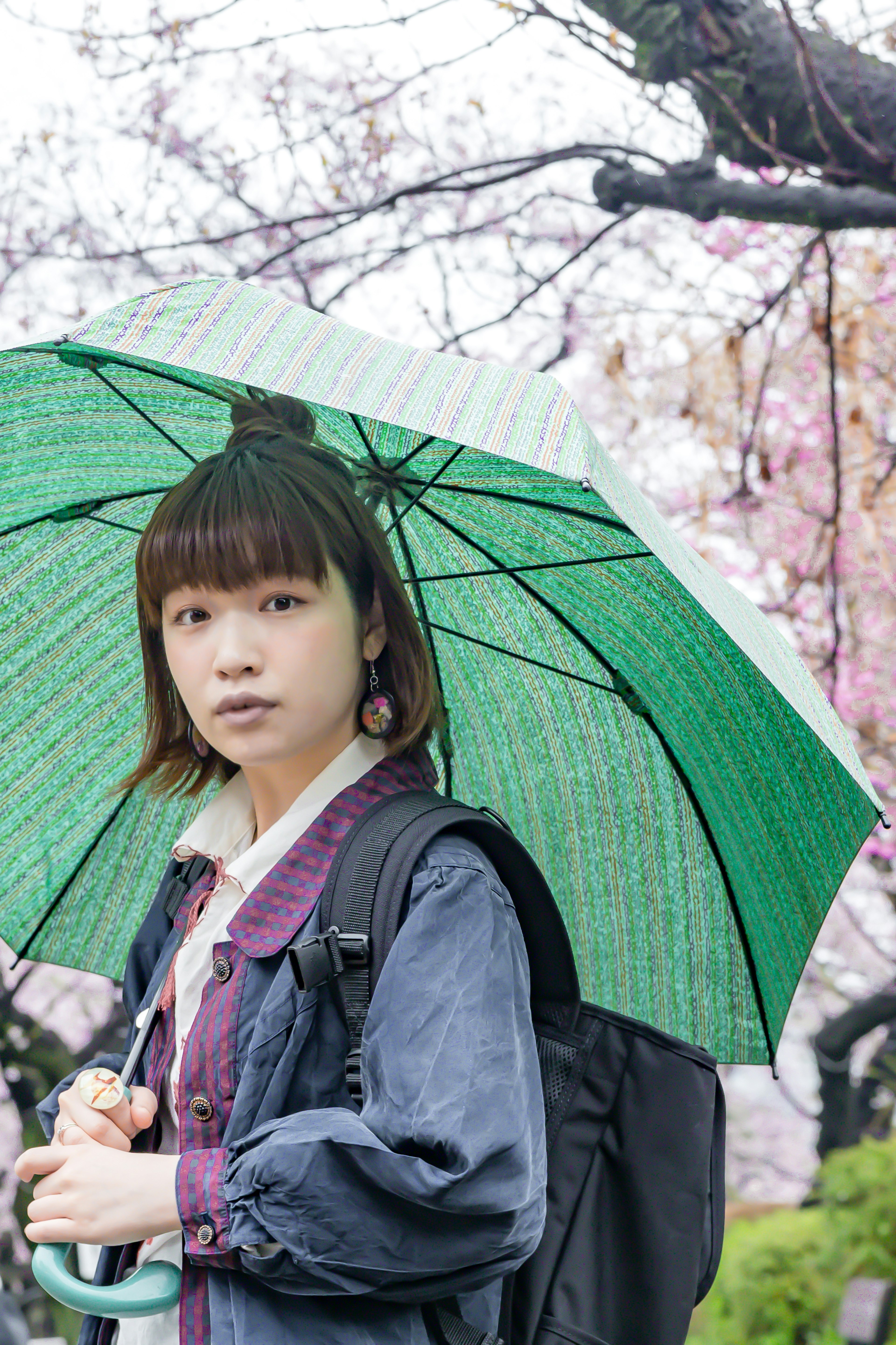 Une femme tenant un parapluie vert se tenant sous des cerisiers en fleurs