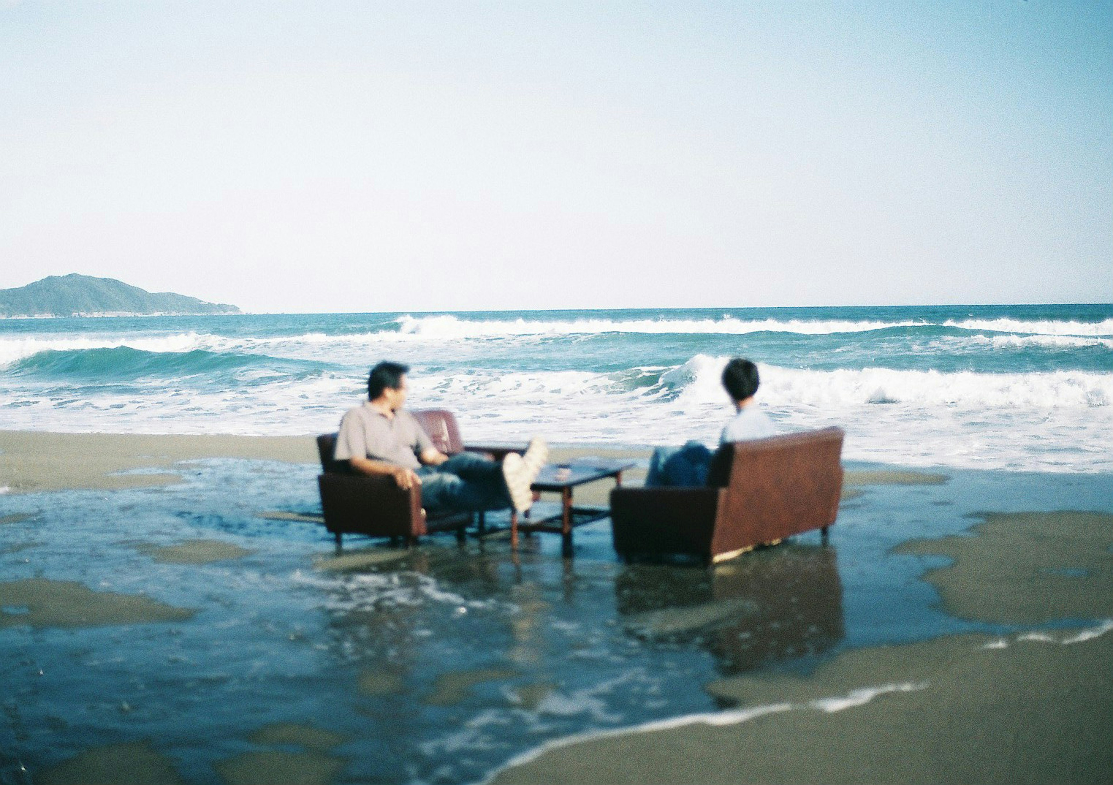 Two men sitting on sofas by the ocean with a table