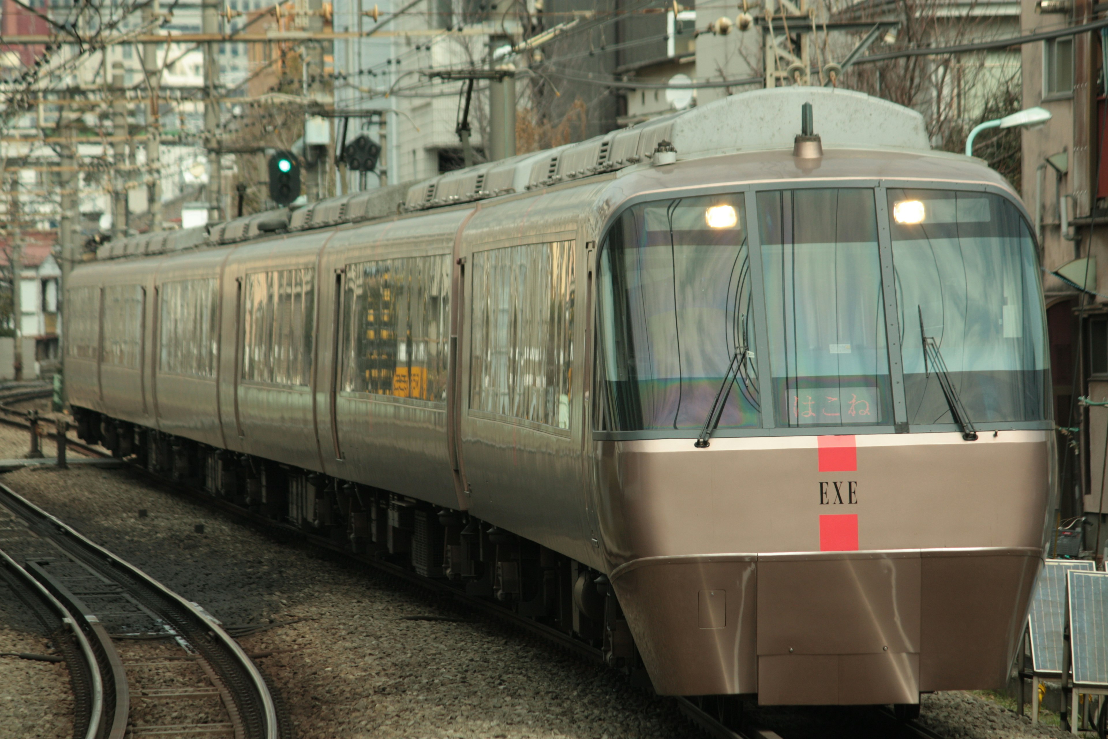 A silver train running on tracks with a green signal in the background