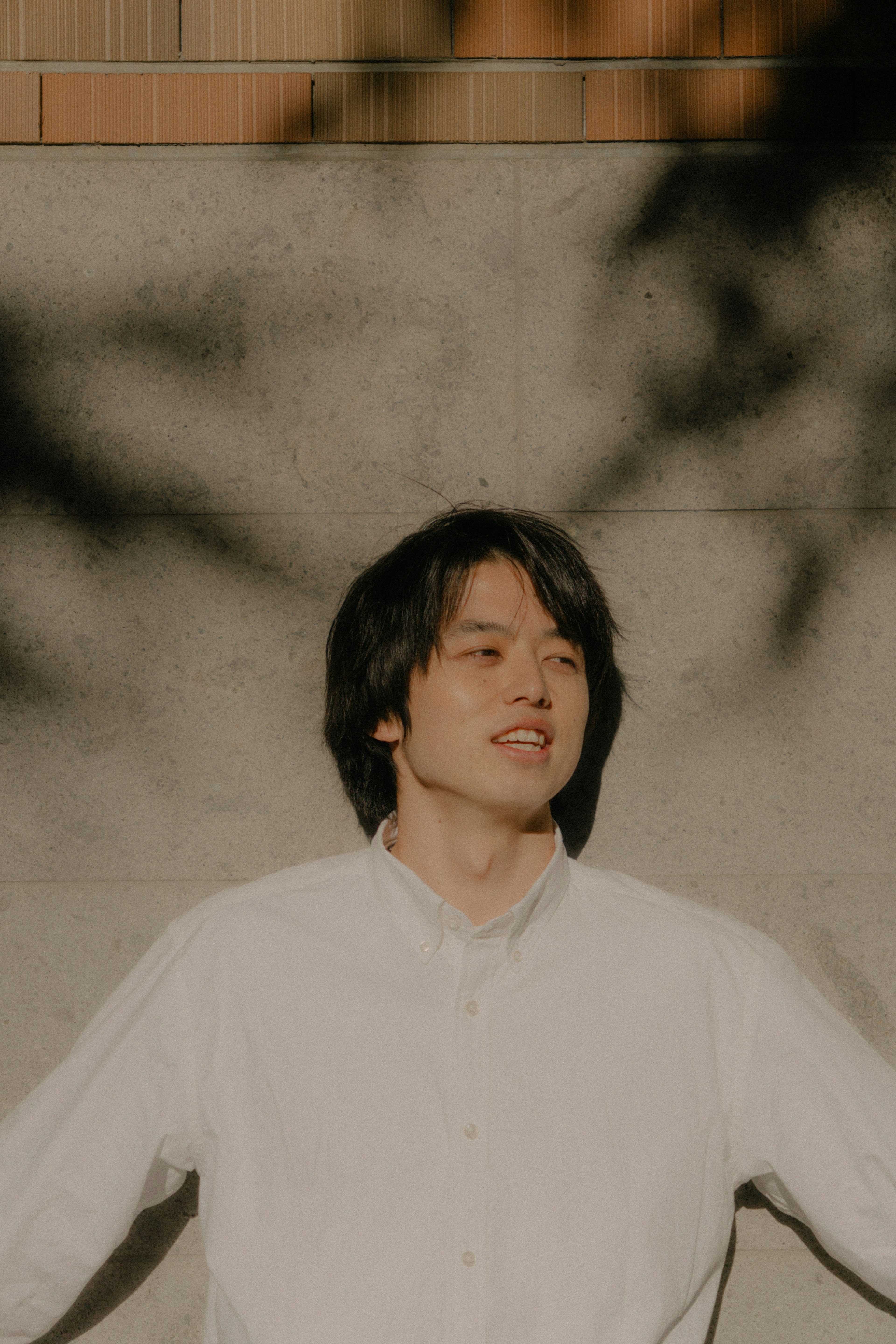 A man in a white shirt standing with arms open against a wall