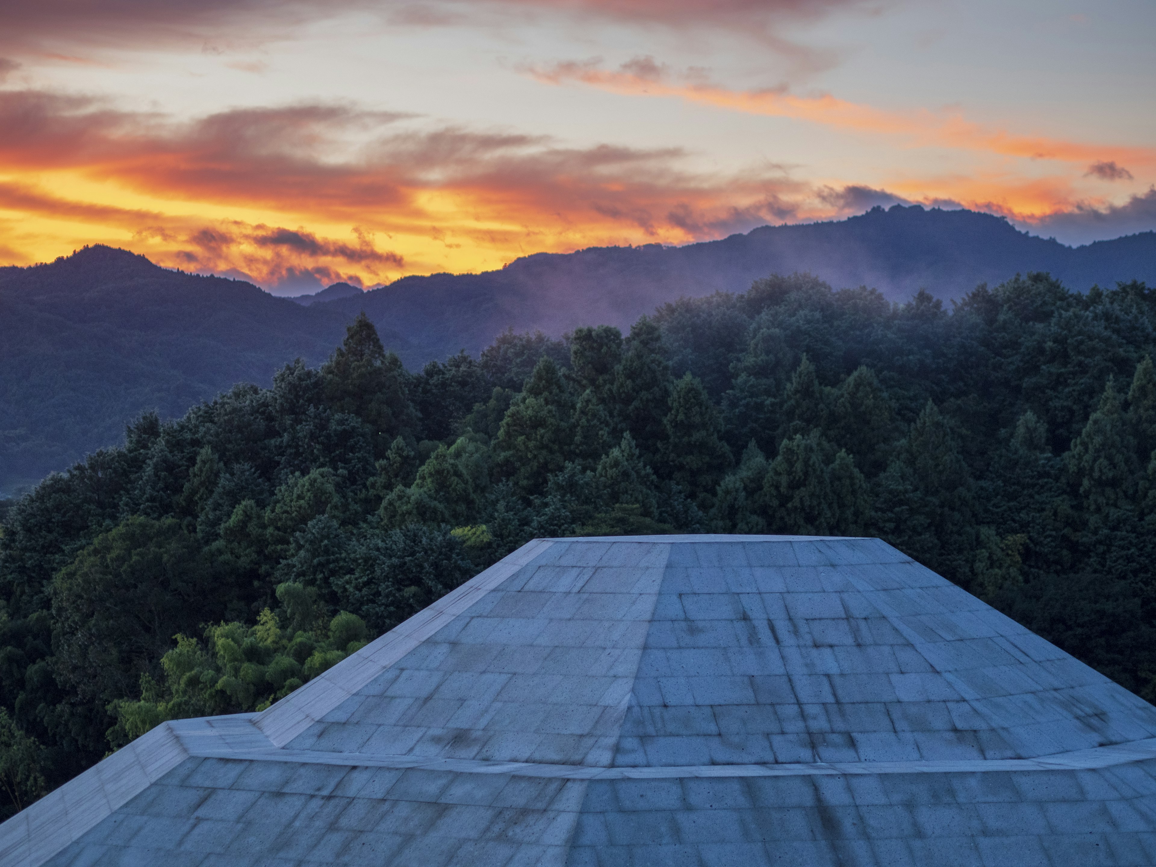 View from a concrete structure overlooking mountains and forest at sunset