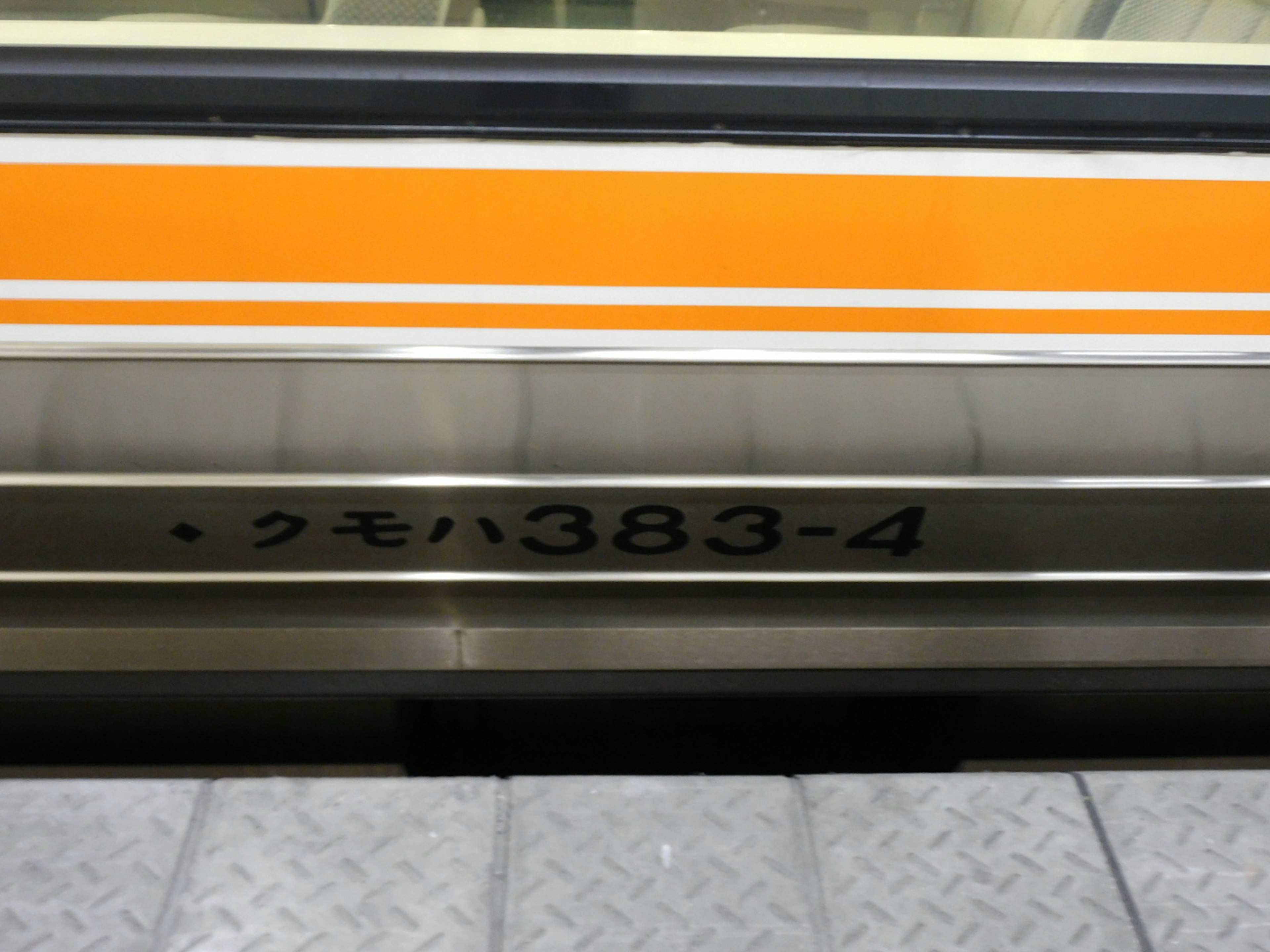 The side of a train featuring an orange stripe with the number Kumoha 383-4