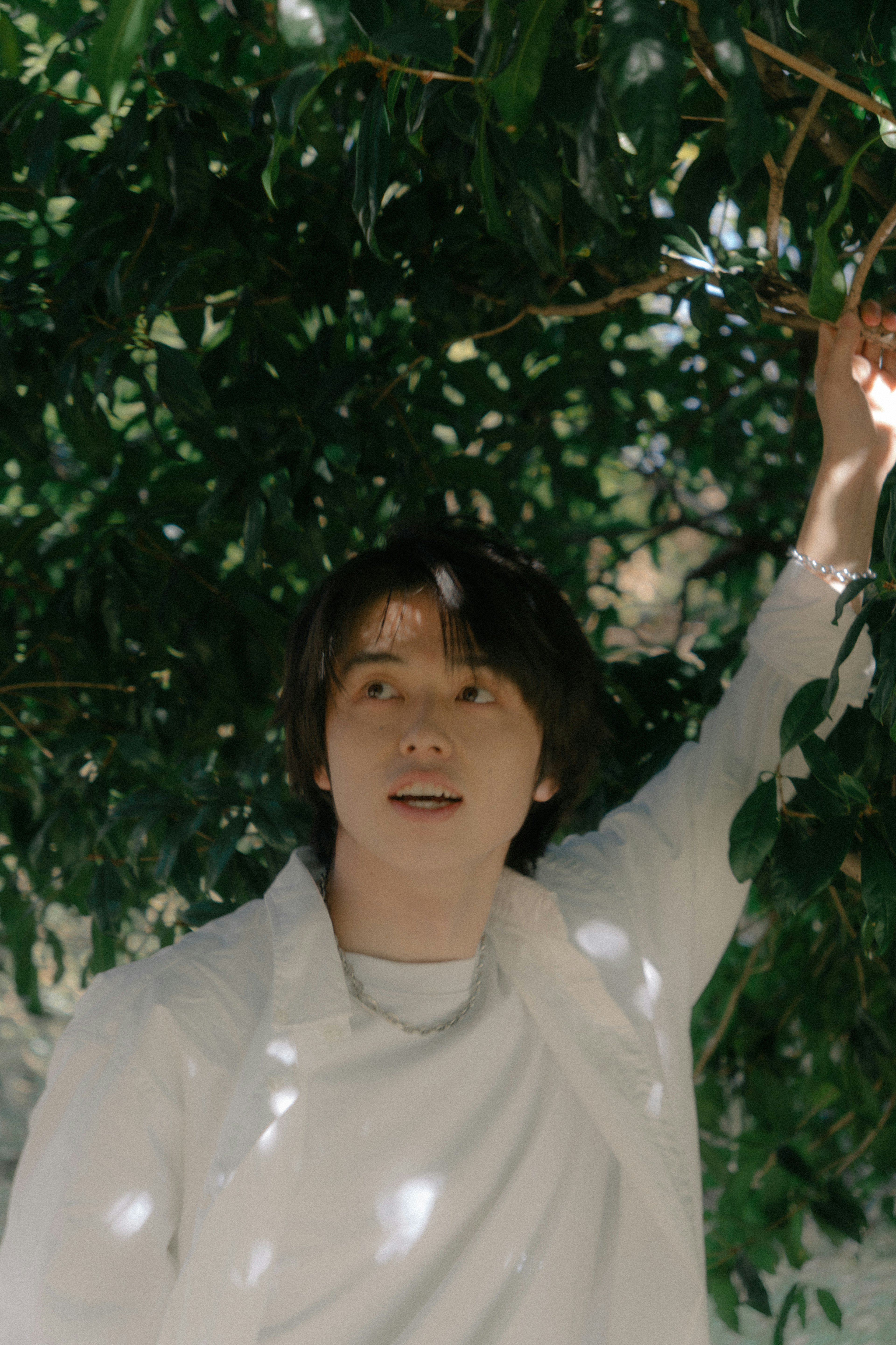 Portrait of a man standing under tree leaves wearing a white outfit