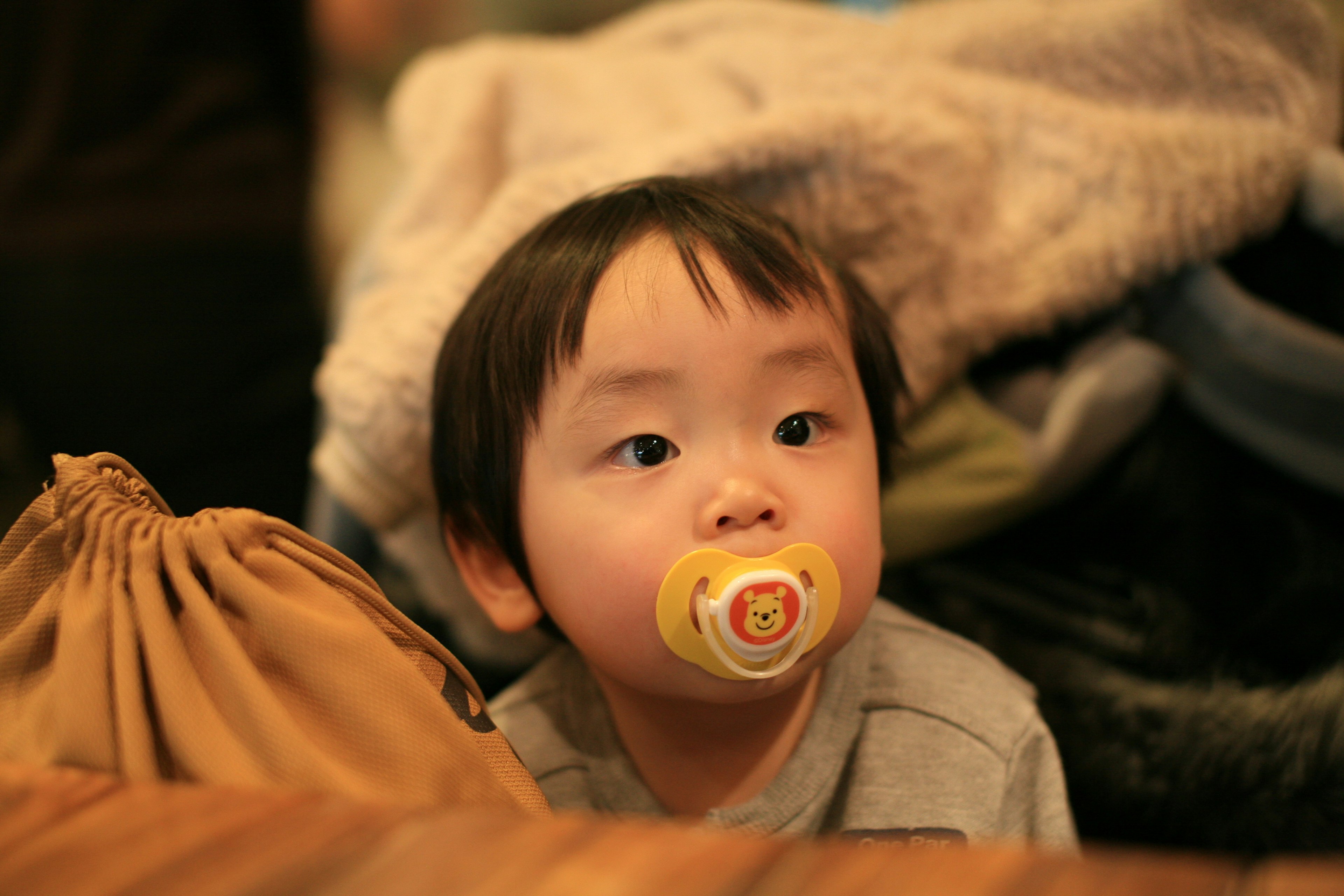 A child with a pacifier surrounded by soft blankets and fabric