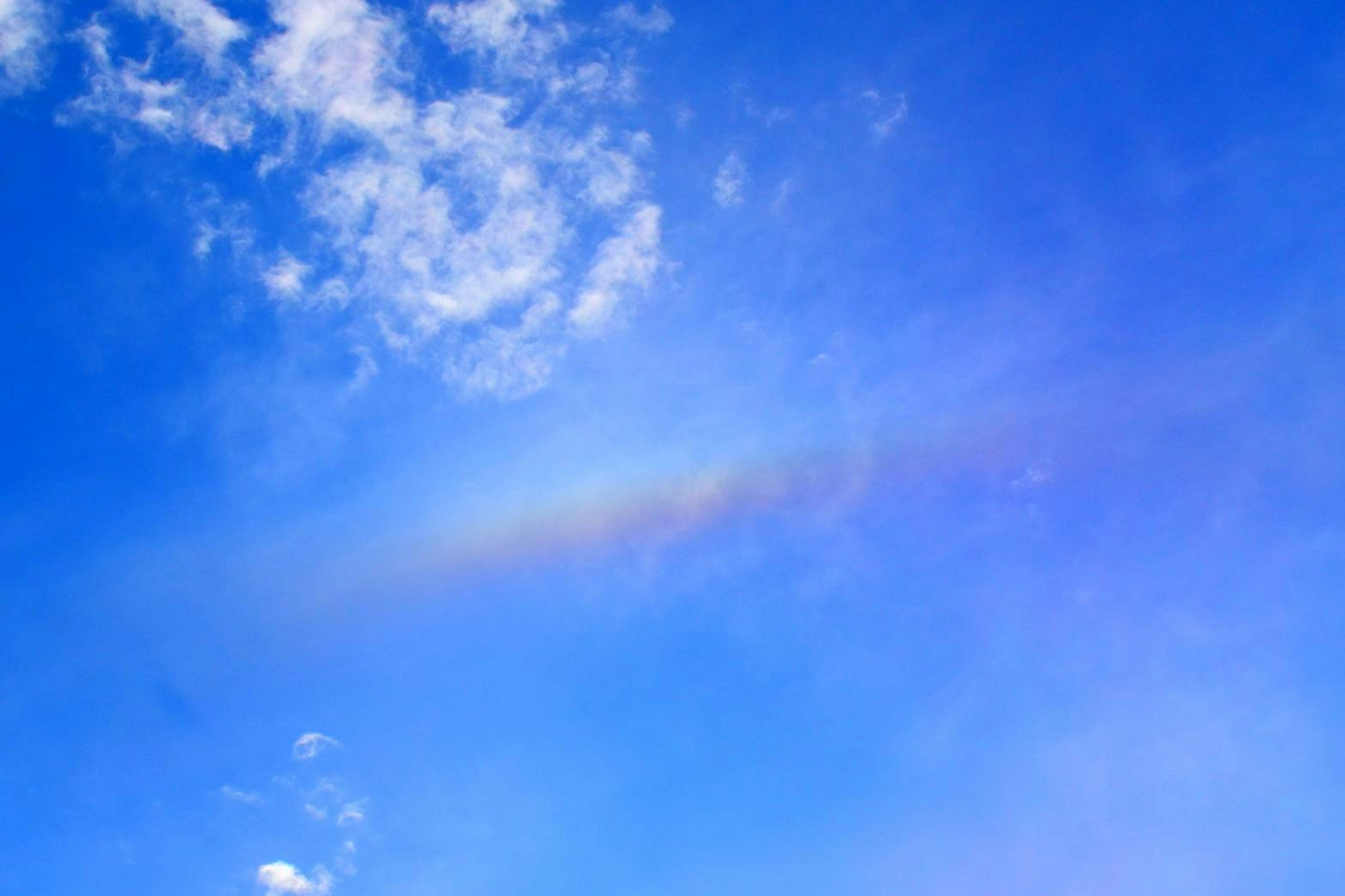 Faint rainbow arching across a bright blue sky with white clouds