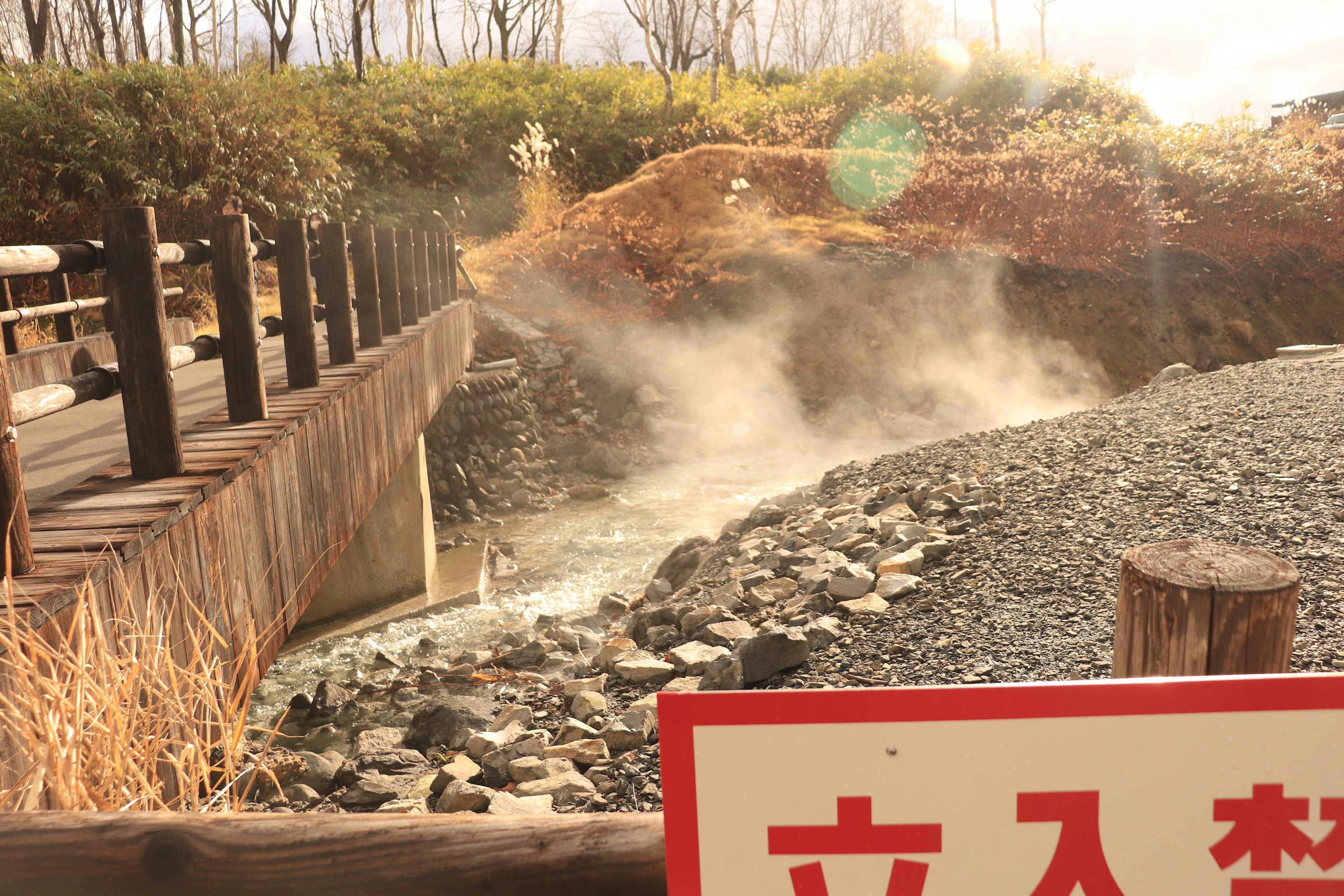 温泉地の蒸気が立ち上る川と木製の橋の風景