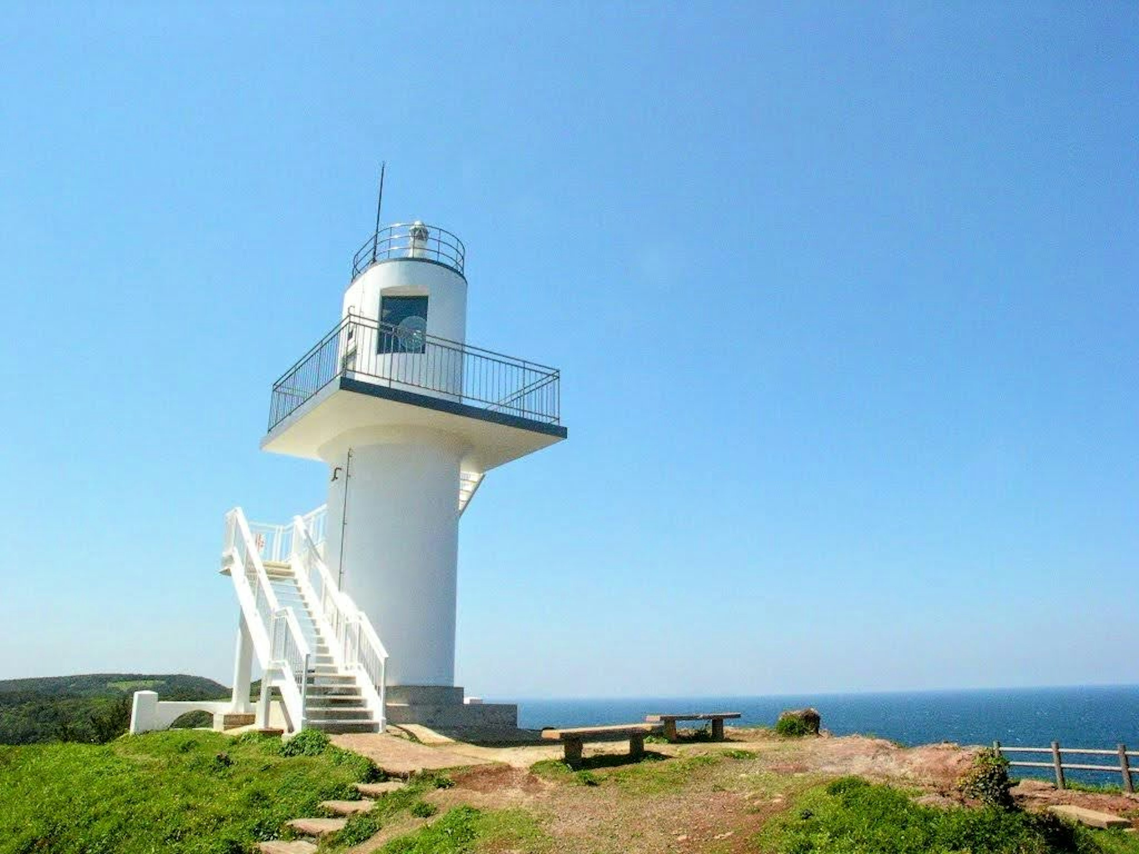 A white lighthouse standing against a blue sky and ocean backdrop