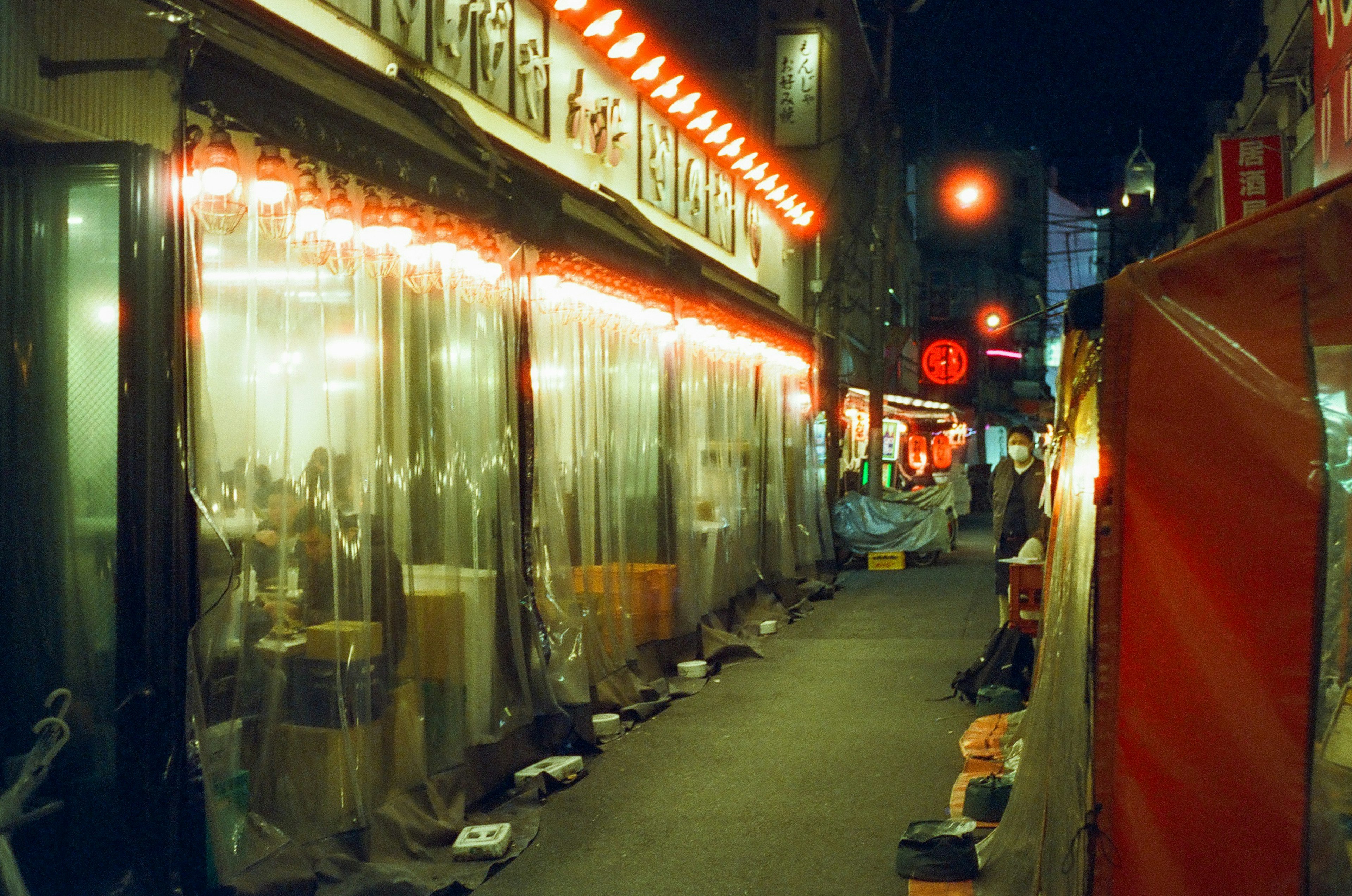 Vue de rue nocturne avec des extérieurs de restaurant éclairés en rouge et des couvertures transparentes