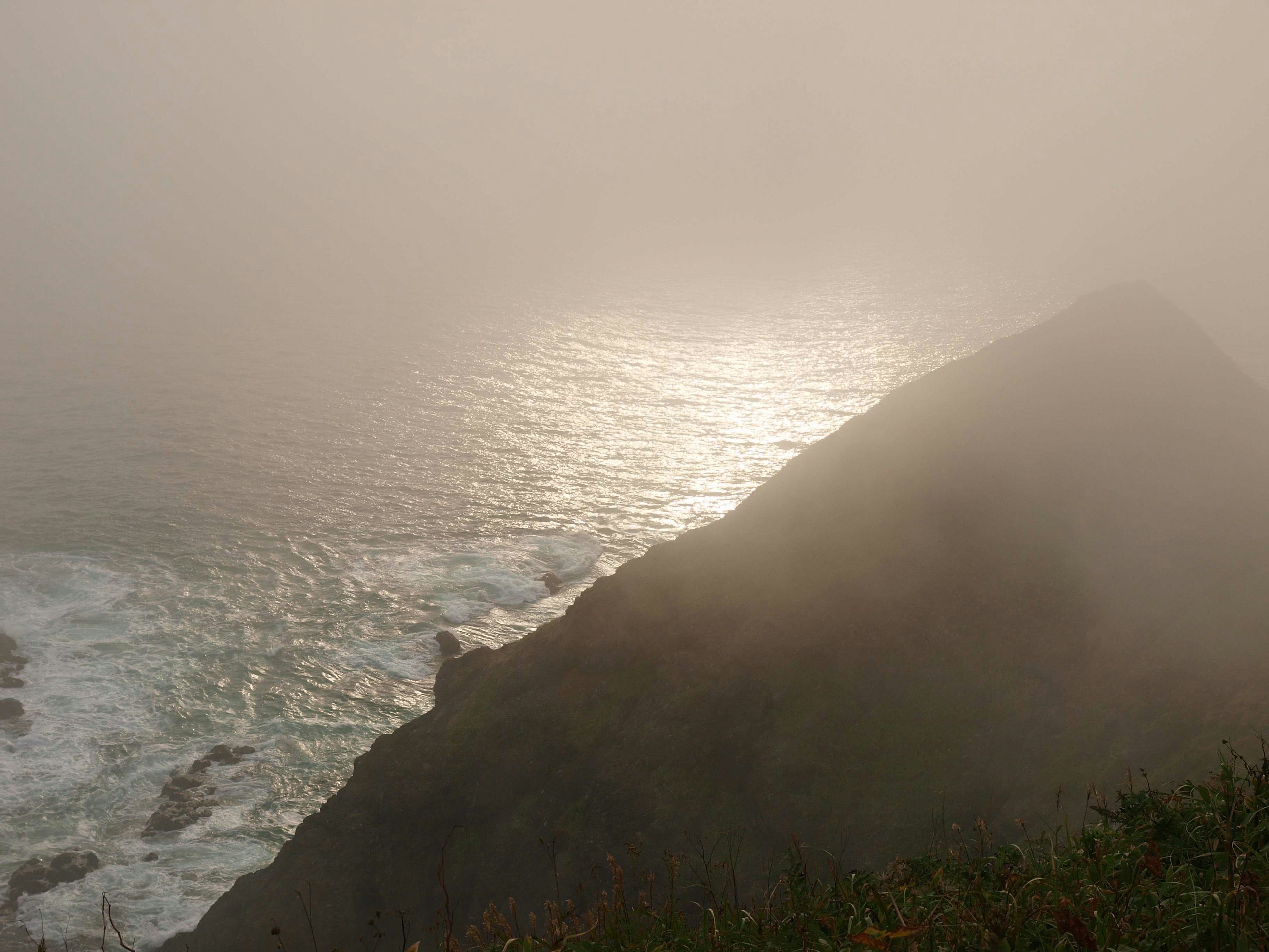 Escena costera neblinosa con olas y reflejos de luz en el agua