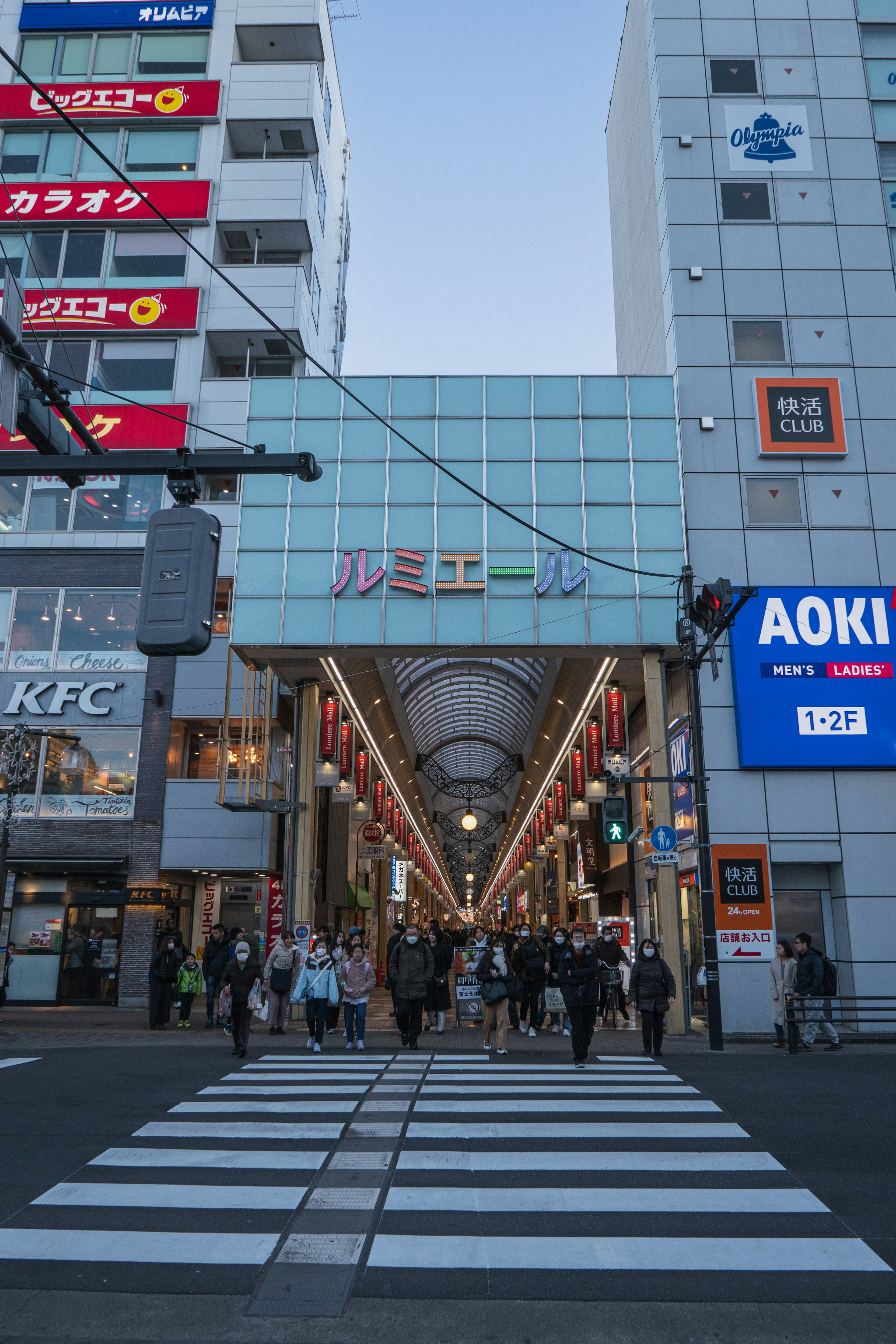 Folla di persone che cammina verso l'ingresso di un'arcade commerciale con edifici commerciali