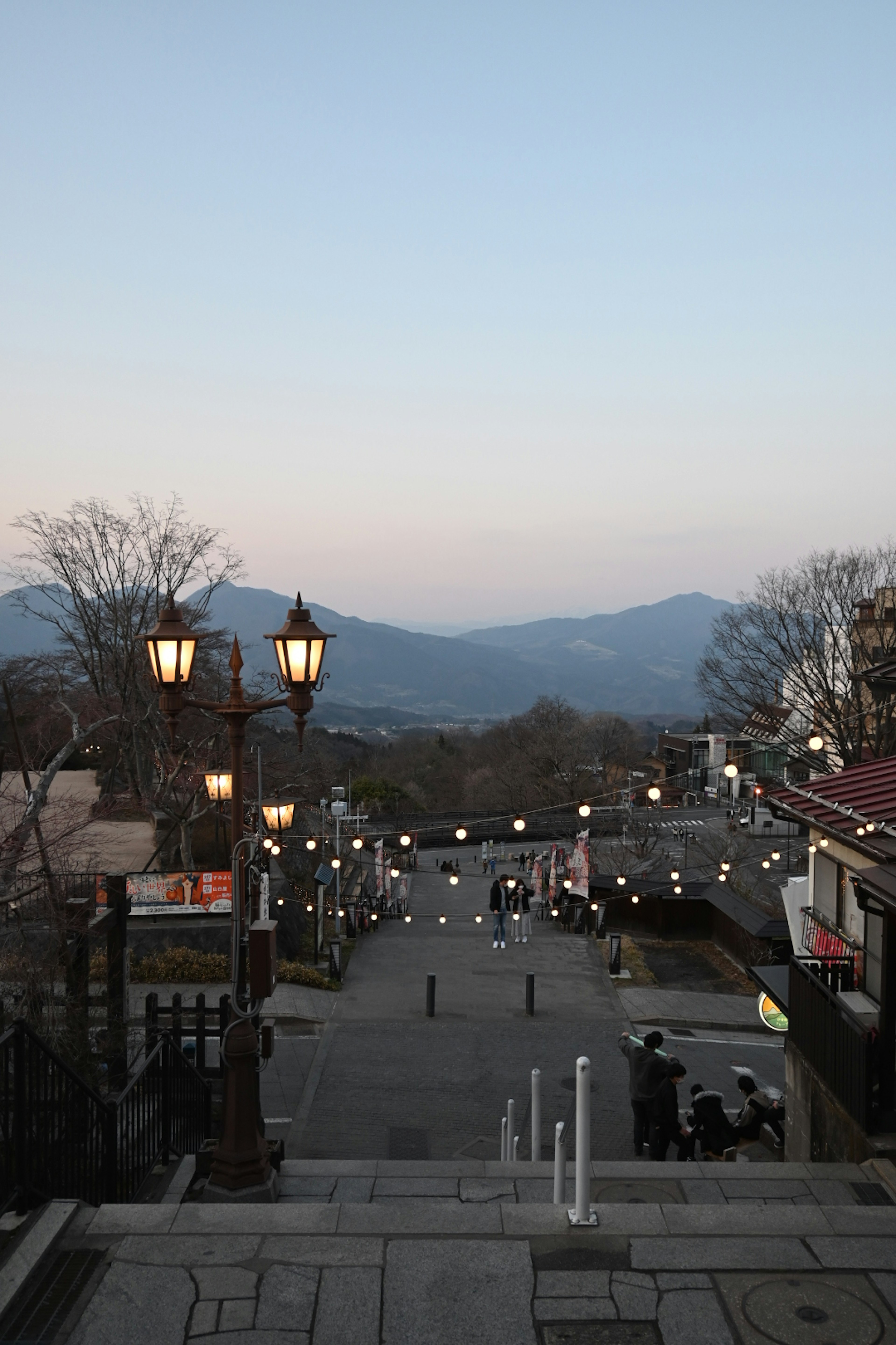 Vista de una escalera de piedra que conduce a una calle con faroles y montañas de fondo al anochecer