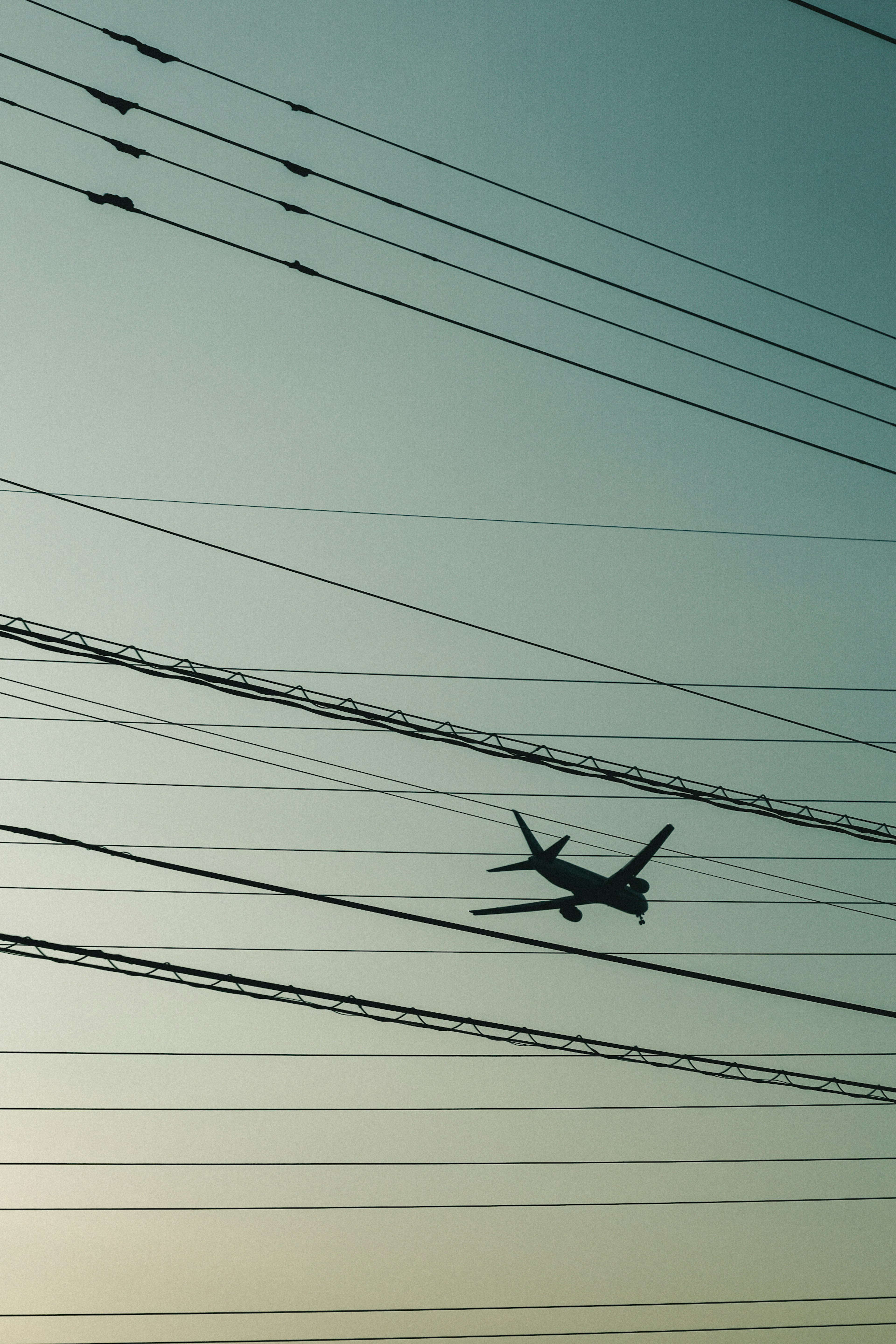 飛行機が電線の間を飛んでいるシルエットの風景