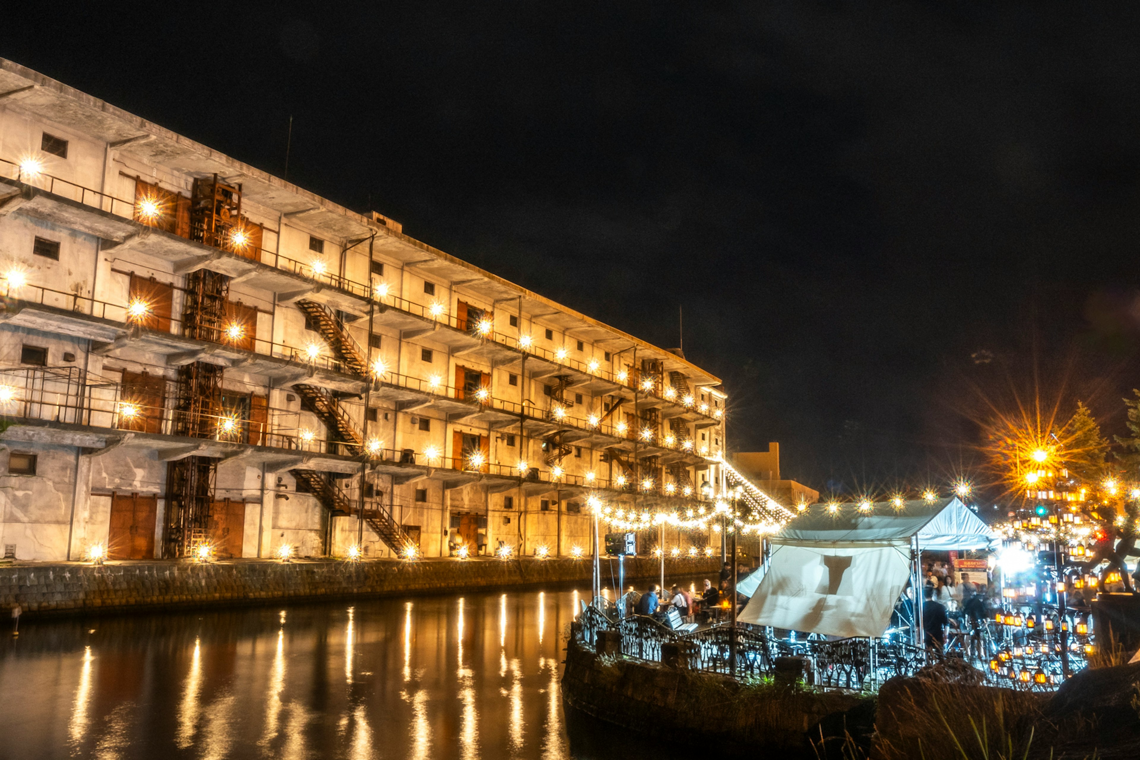 Bâtiment historique au bord de la rivière illuminé la nuit avec un espace événementiel extérieur