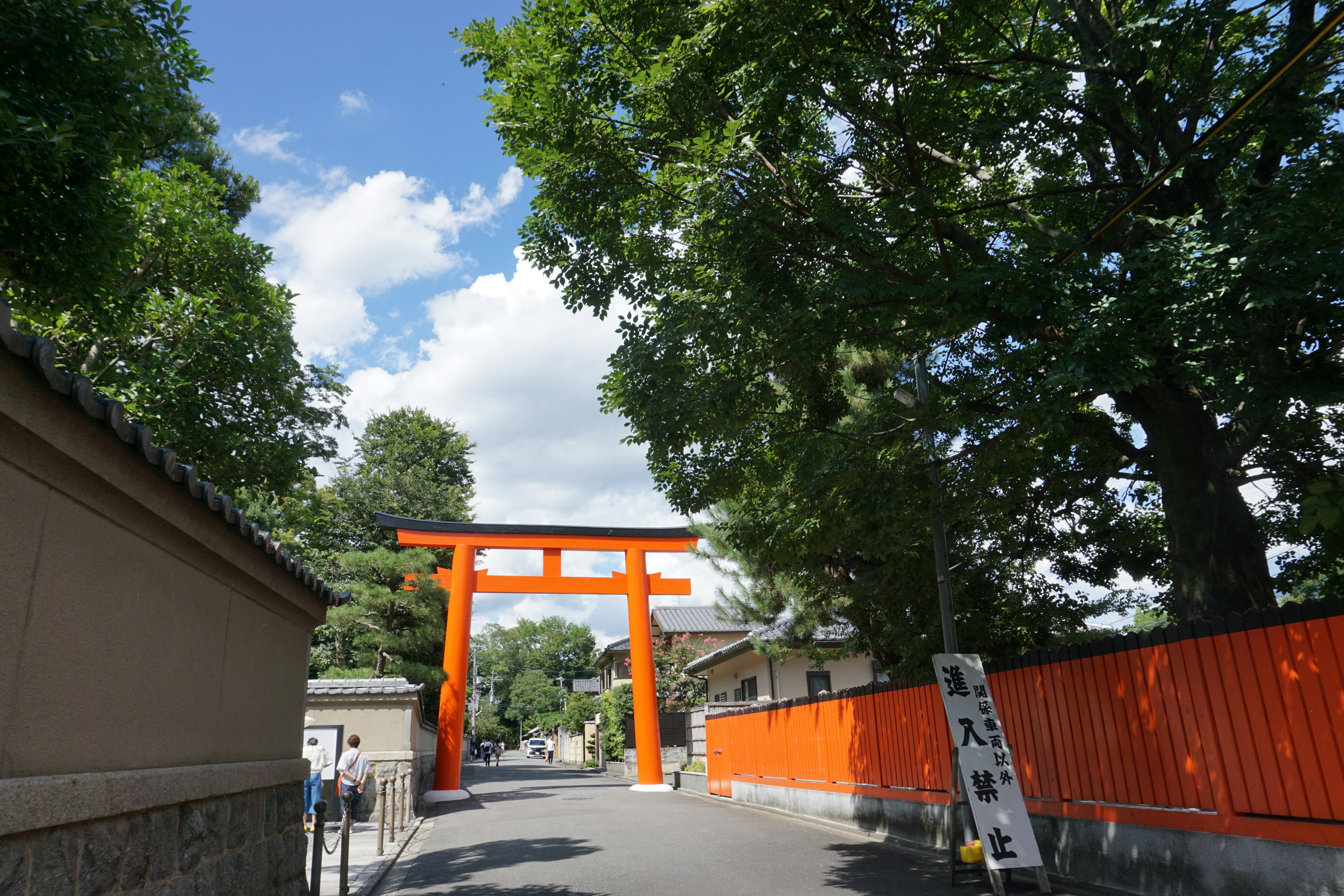 Orange torii gate under a blue sky with lush green trees