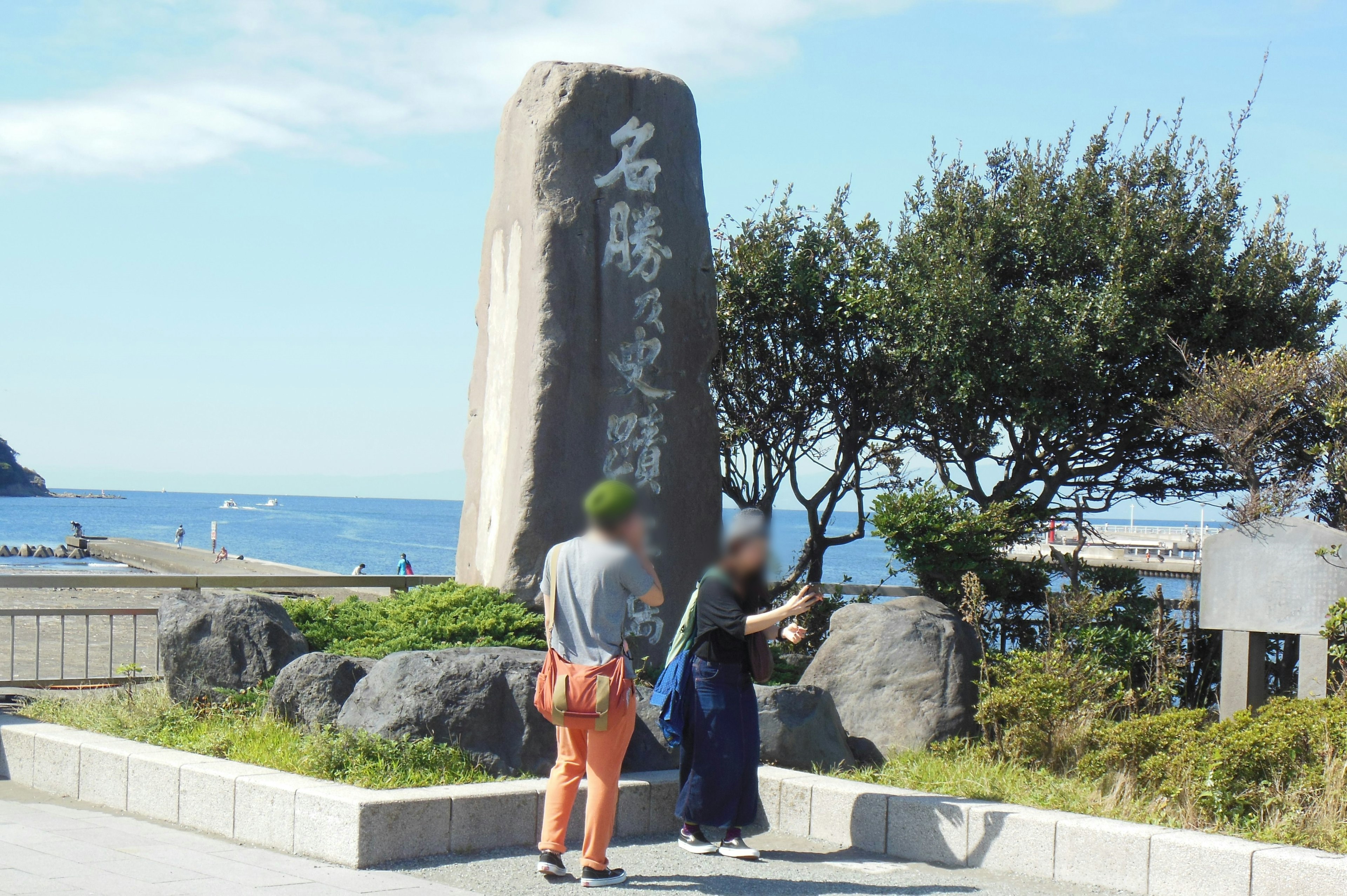 Zwei Personen stehen neben einem großen Steindenkmal am Meer