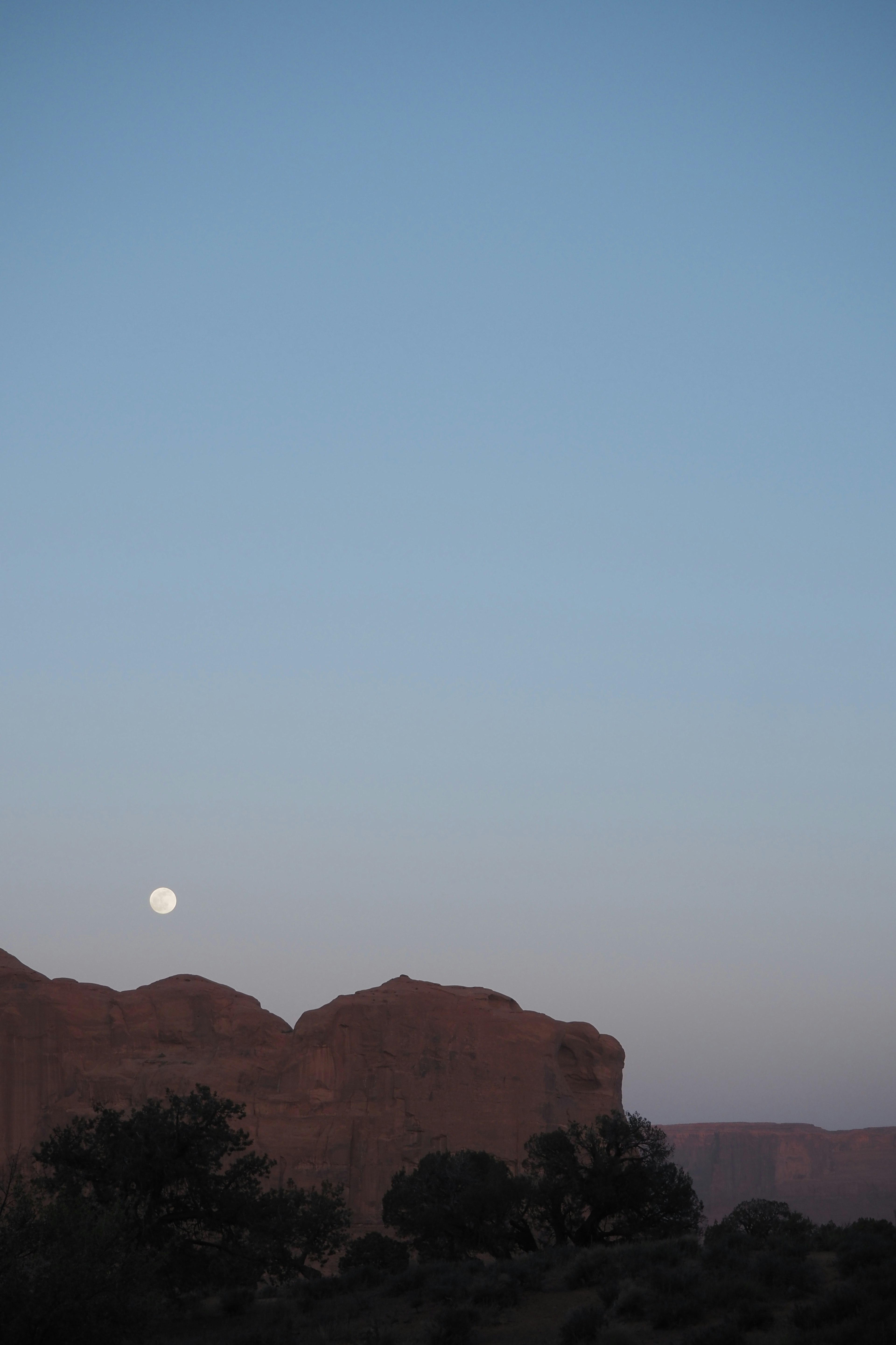 Luna saliendo sobre montañas rojas bajo un cielo azul