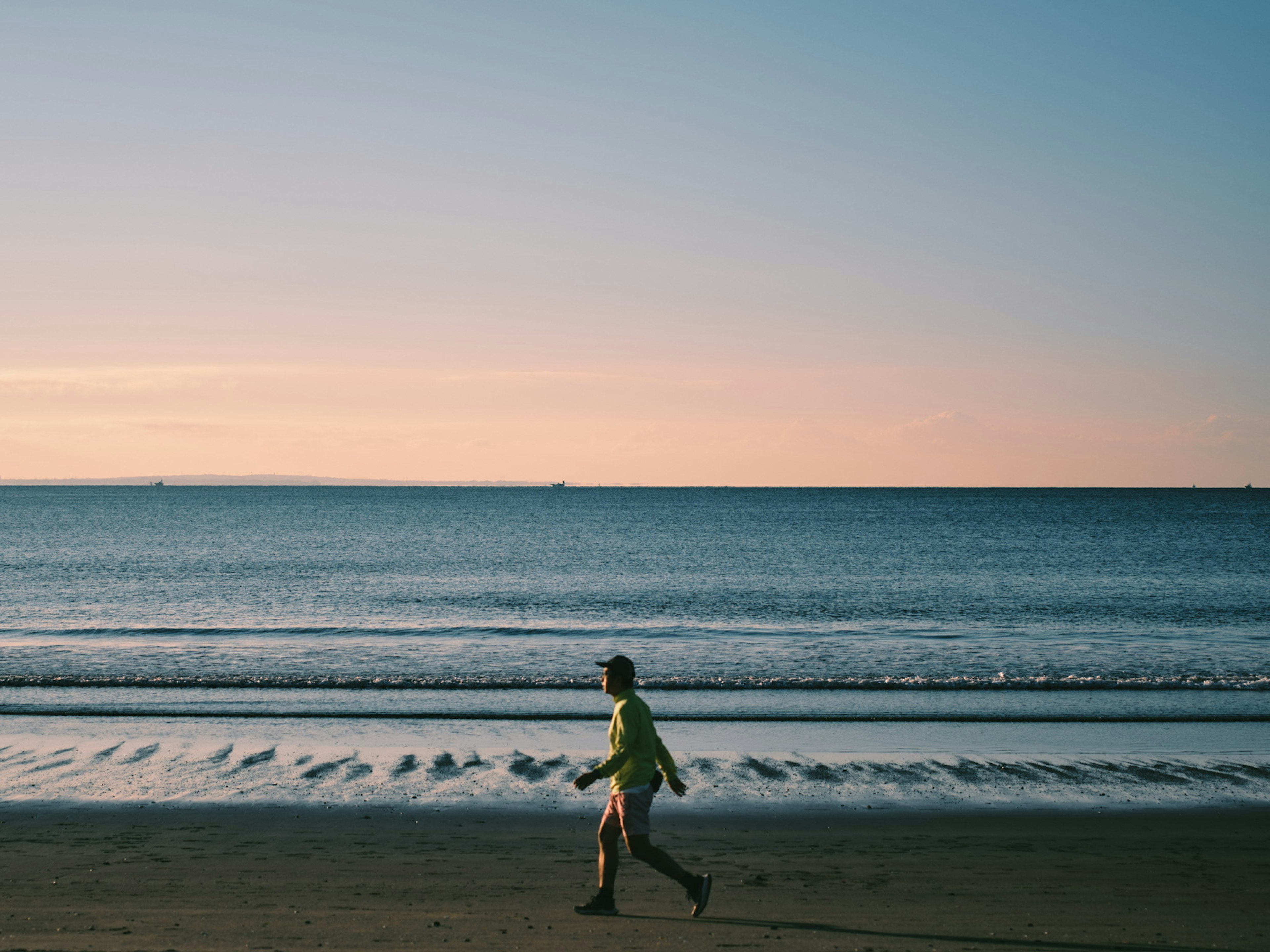 Personne courant le long du rivage avec une mer calme et un coucher de soleil