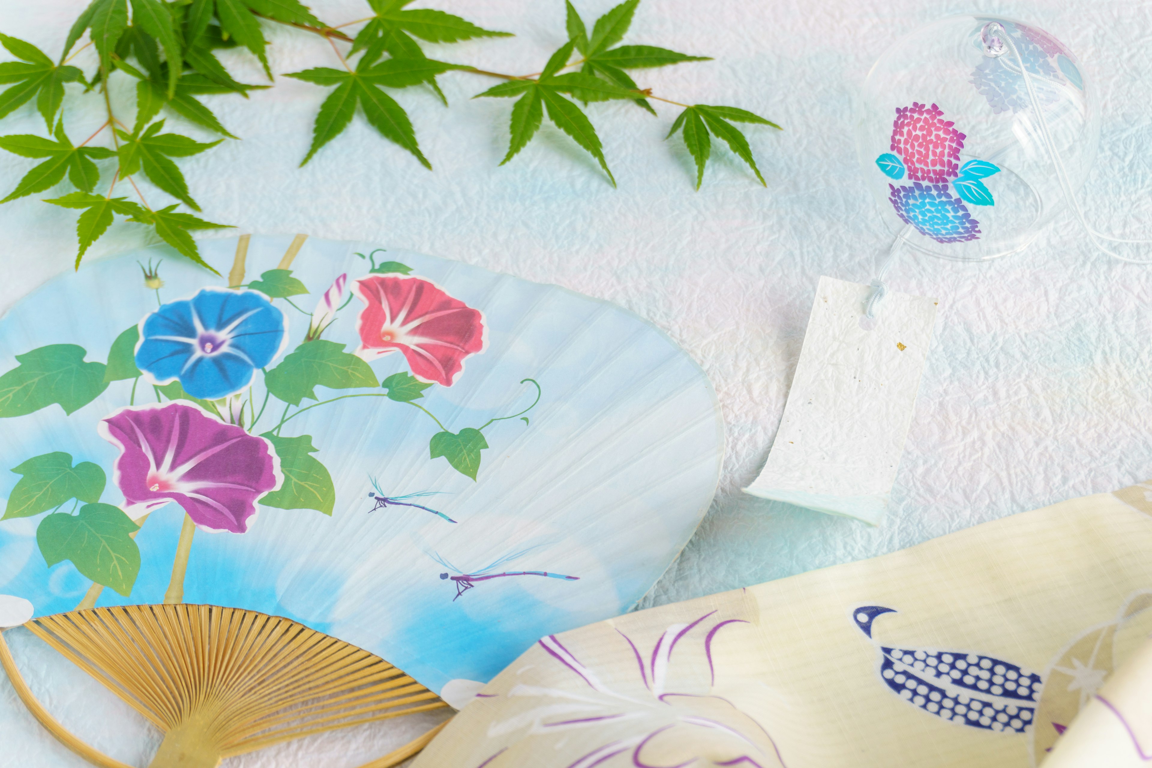 Traditional Japanese fan and glass wind chime with green leaves scattered around