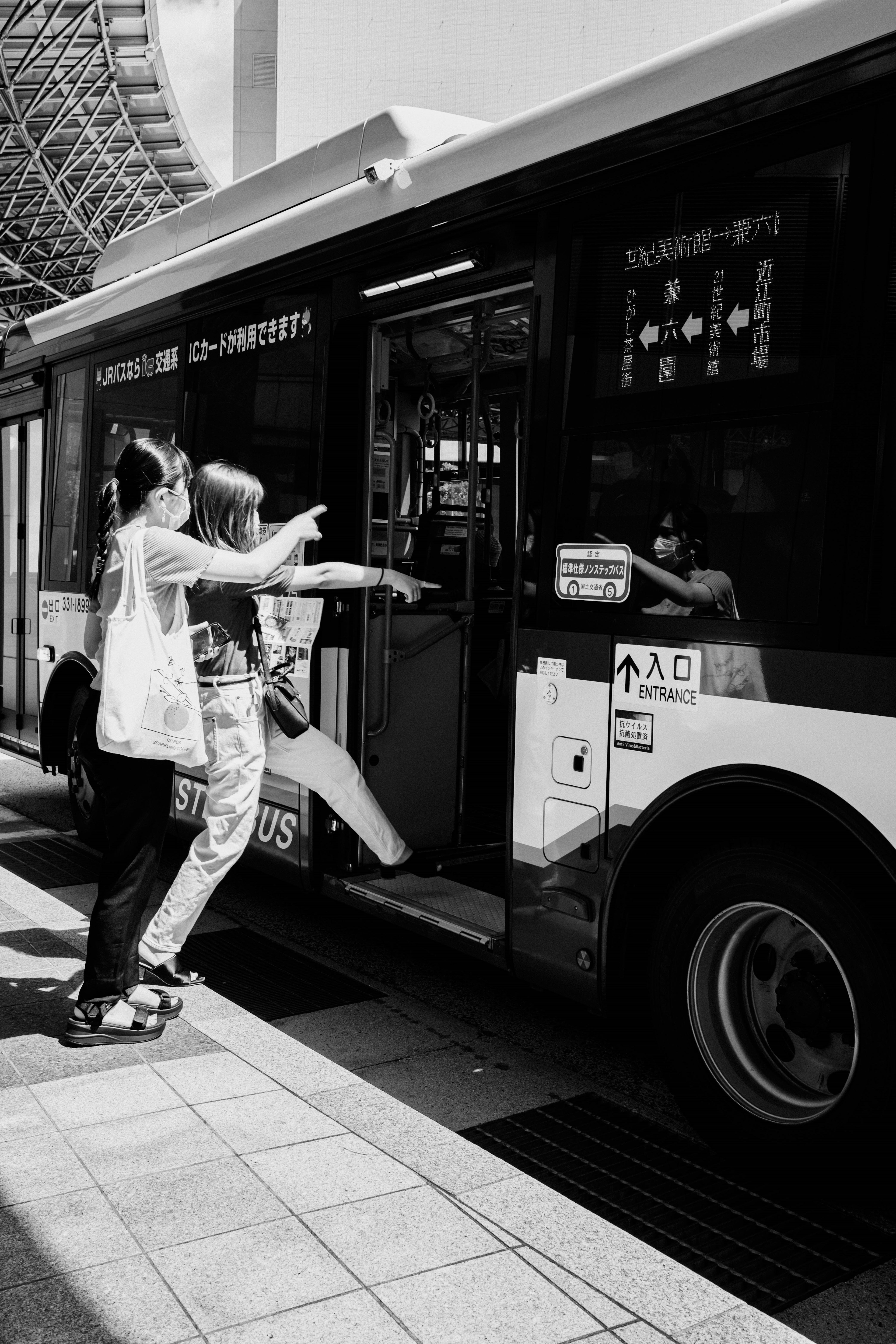 Zwei Frauen versuchen in einen Bus einzusteigen, eine zeigt mit dem Finger