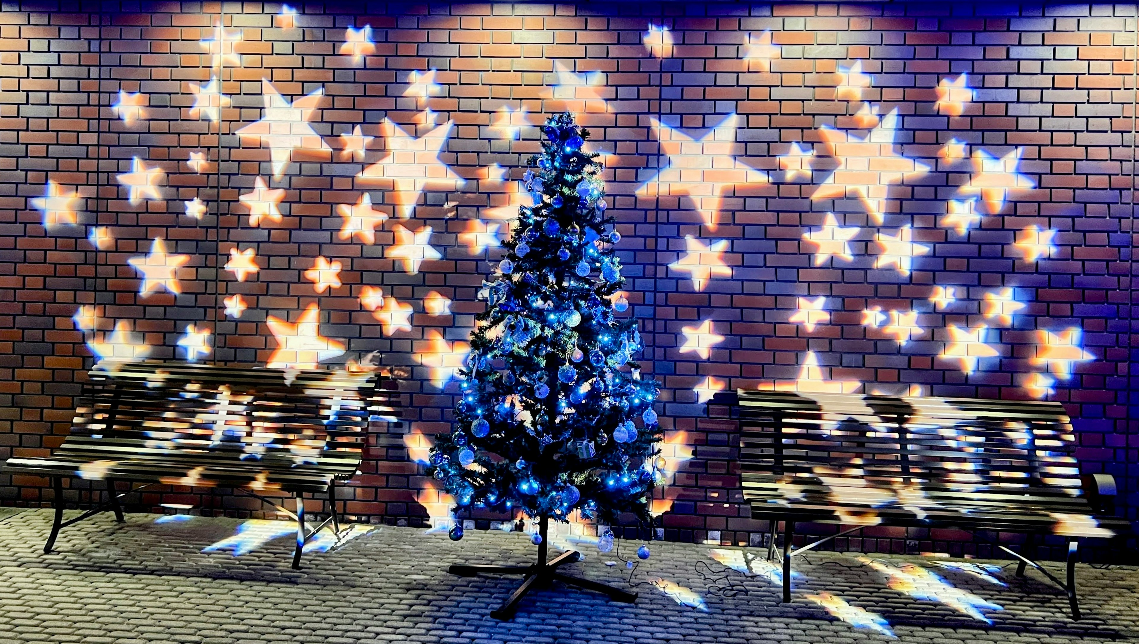 Christmas tree illuminated with star-shaped lights against a brick wall with benches