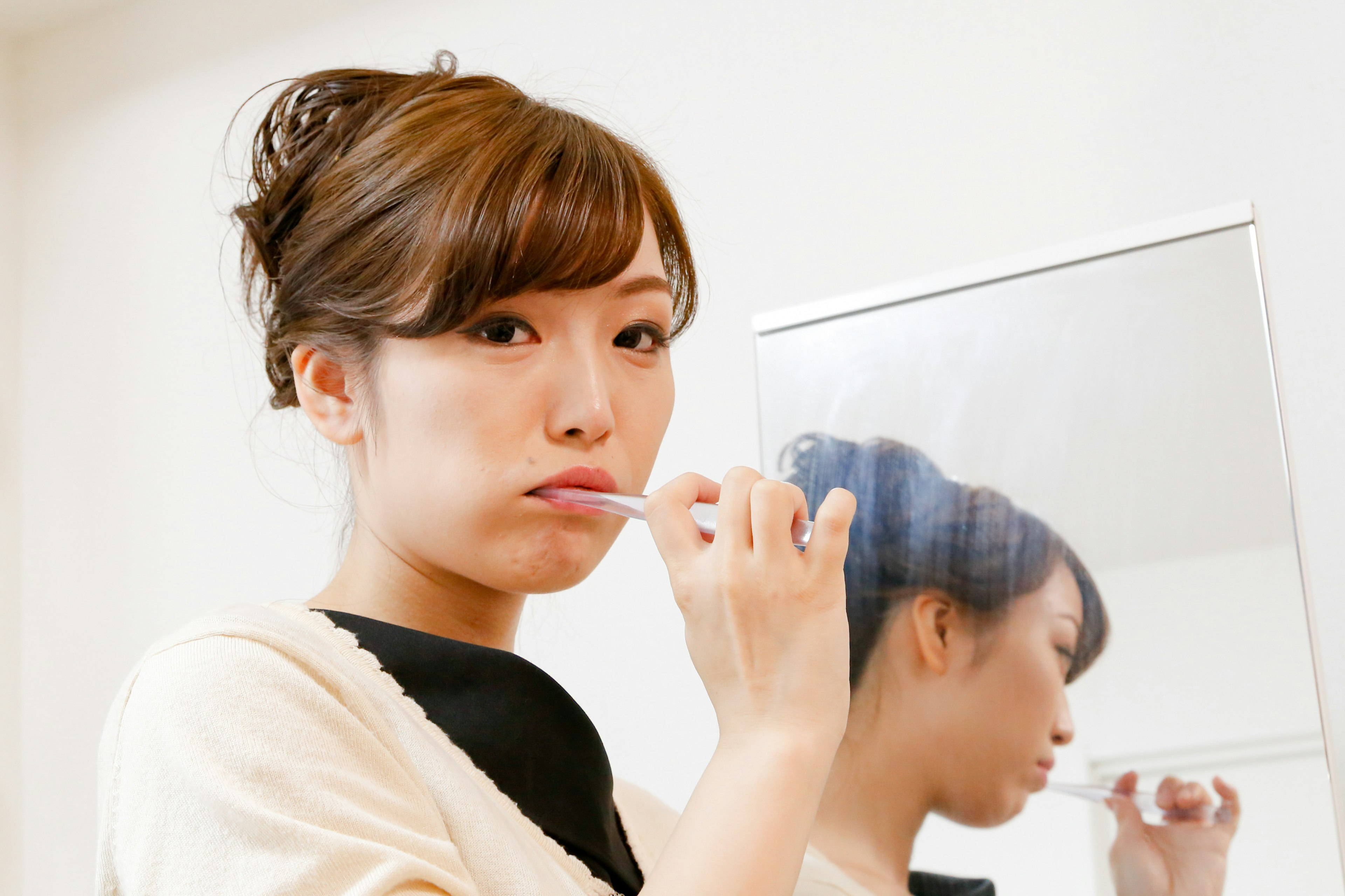 Woman brushing teeth in front of a mirror holding a toothbrush