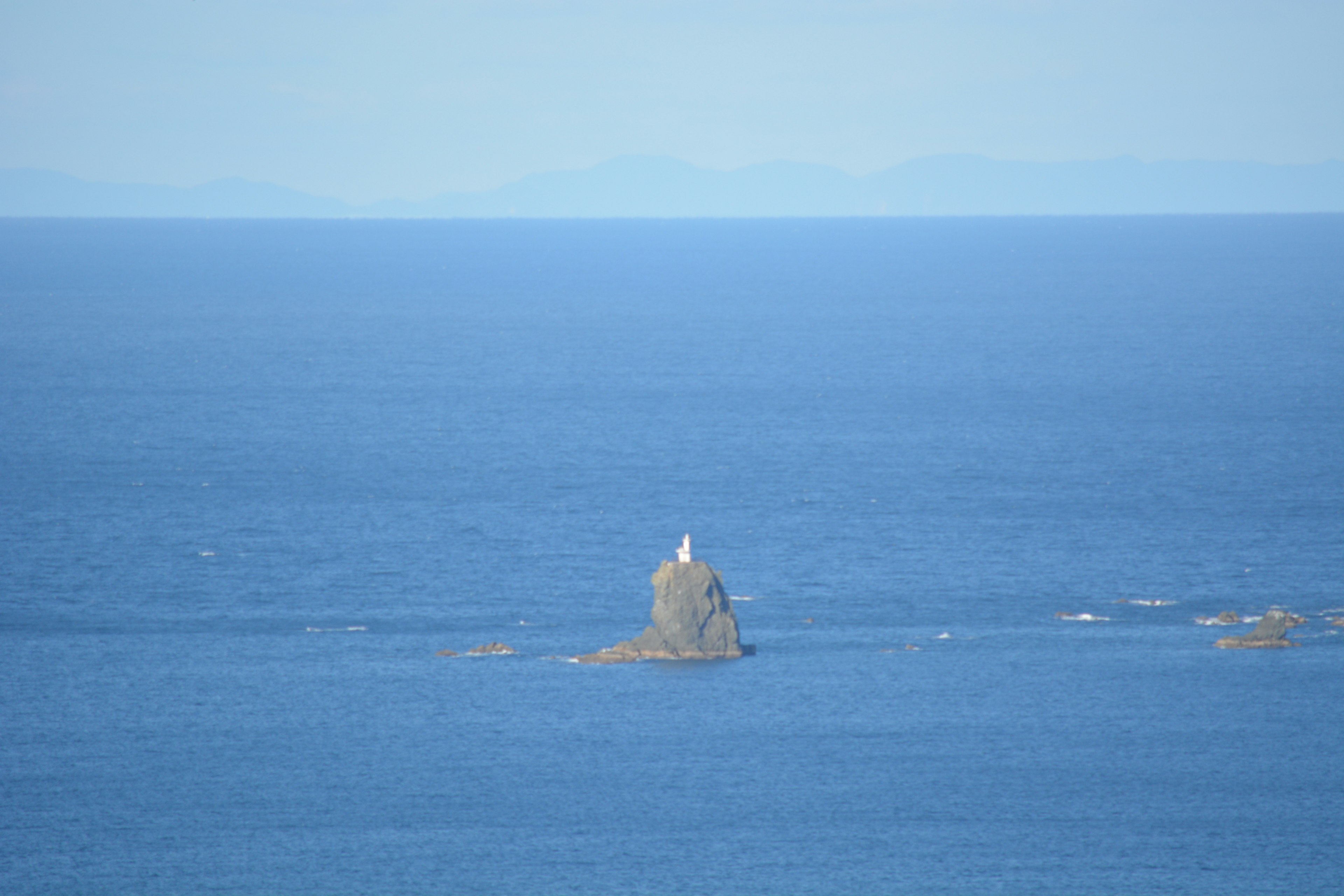 青い海に浮かぶ小さな岩の上に立つ白い灯台